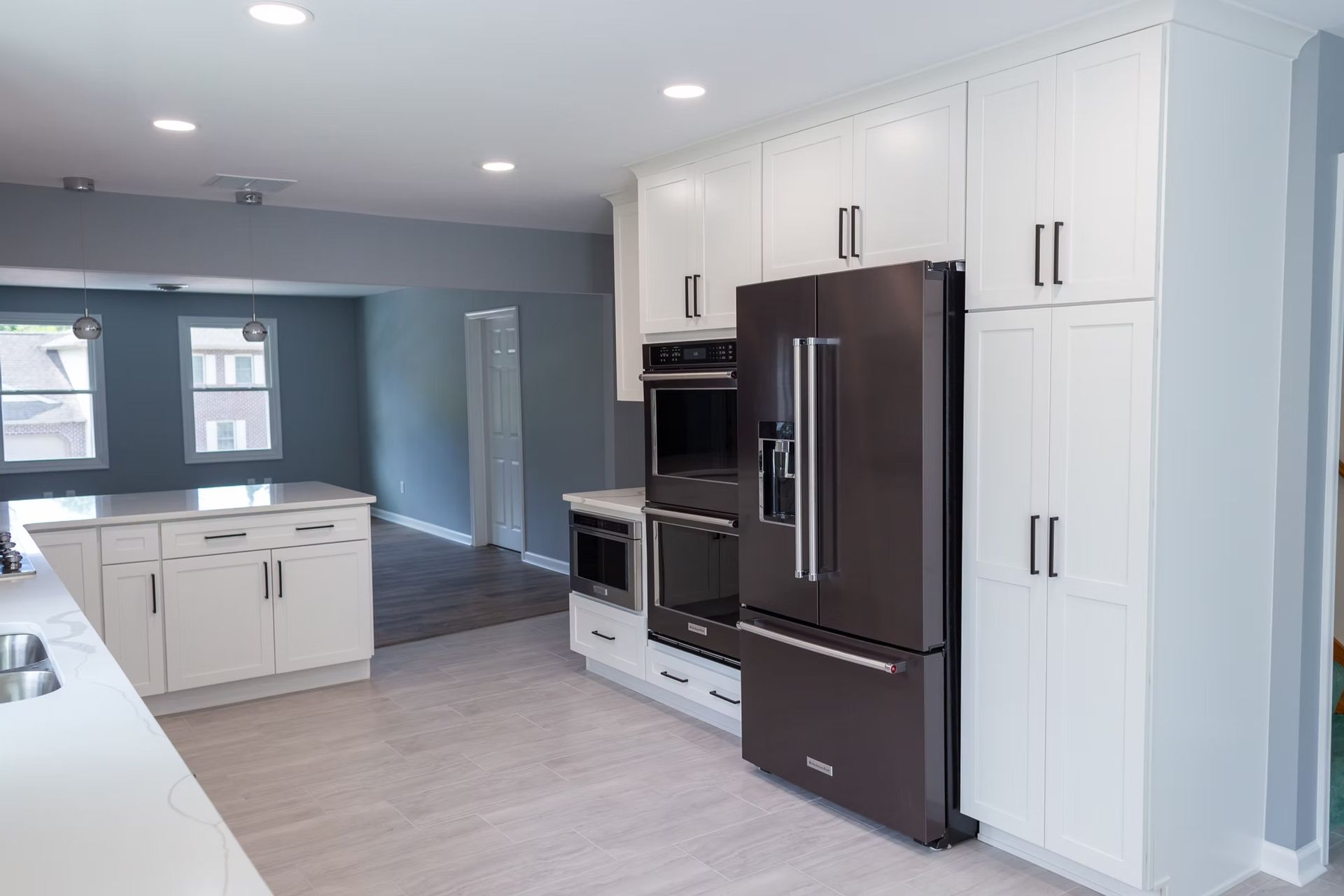 Modern white kitchen with black appliances. Island with cabinets, refrigerator, and ovens.