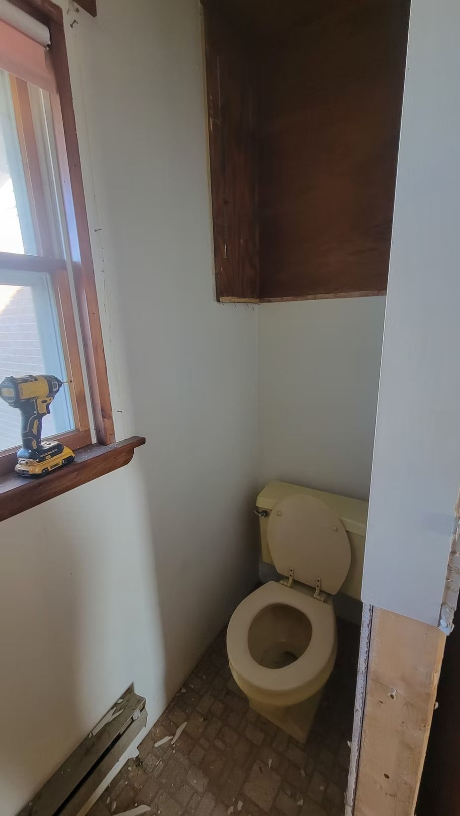 Small, yellow toilet in a cramped bathroom. A brown cabinet hangs above the toilet.