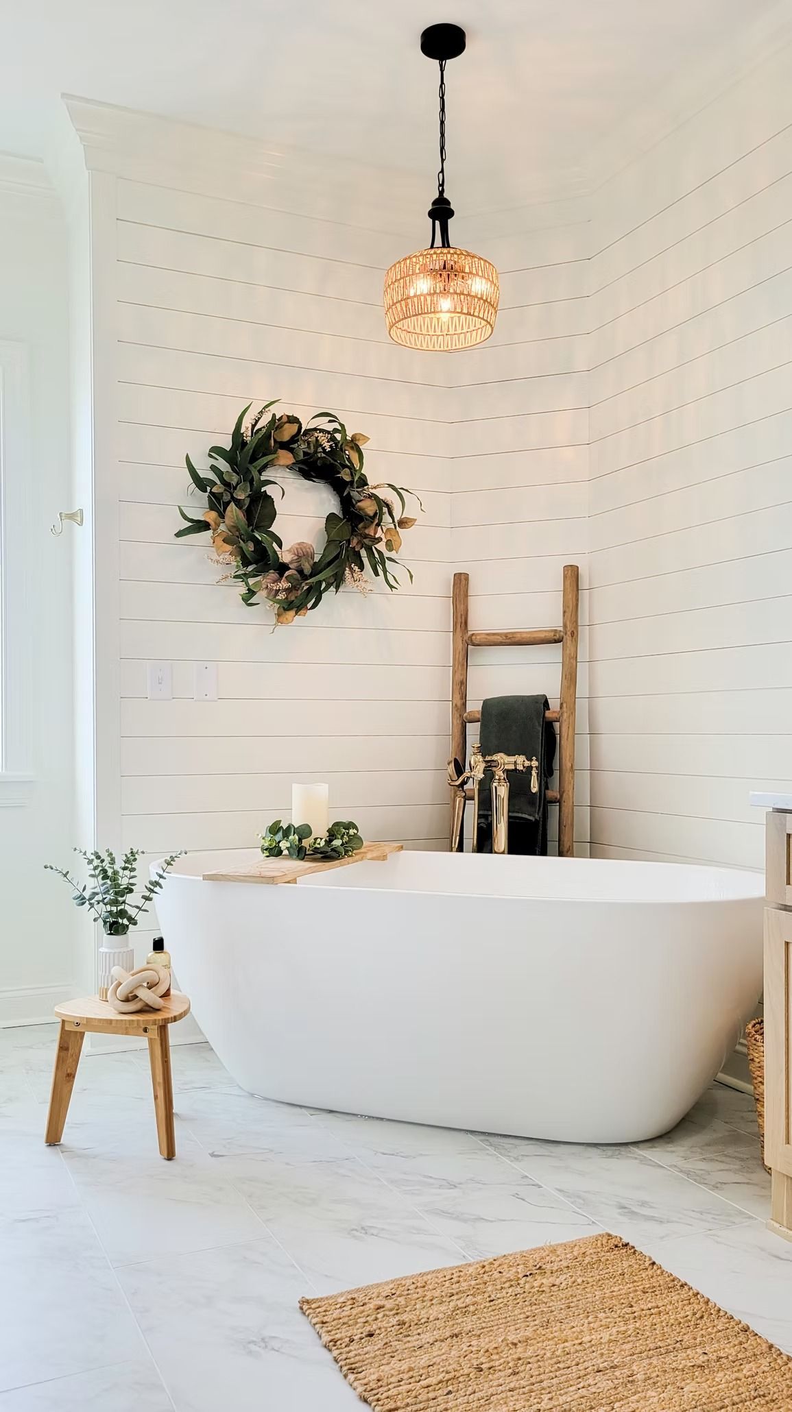 A white bathtub in a bathroom with a wooden ladder, wreath, and decorative lighting.