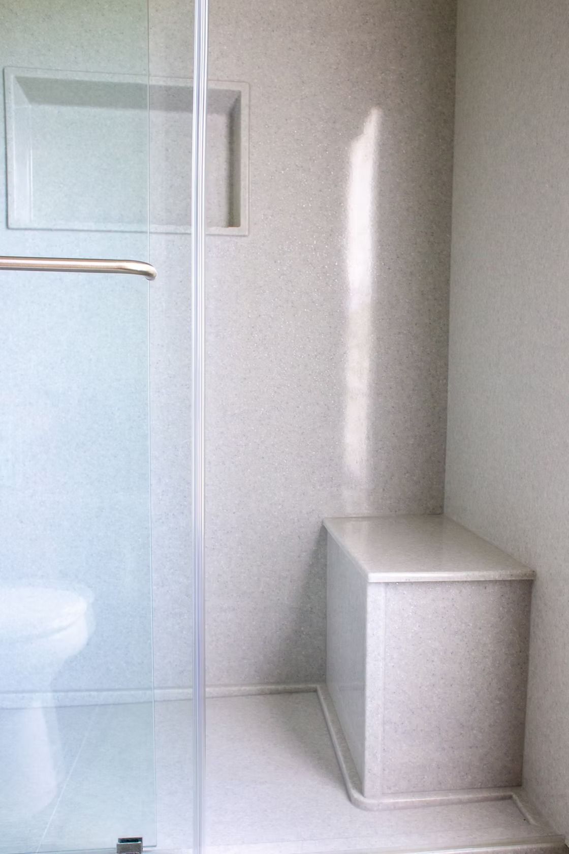 Shower stall with built-in bench, recessed shelves, and glass door, all in speckled gray.