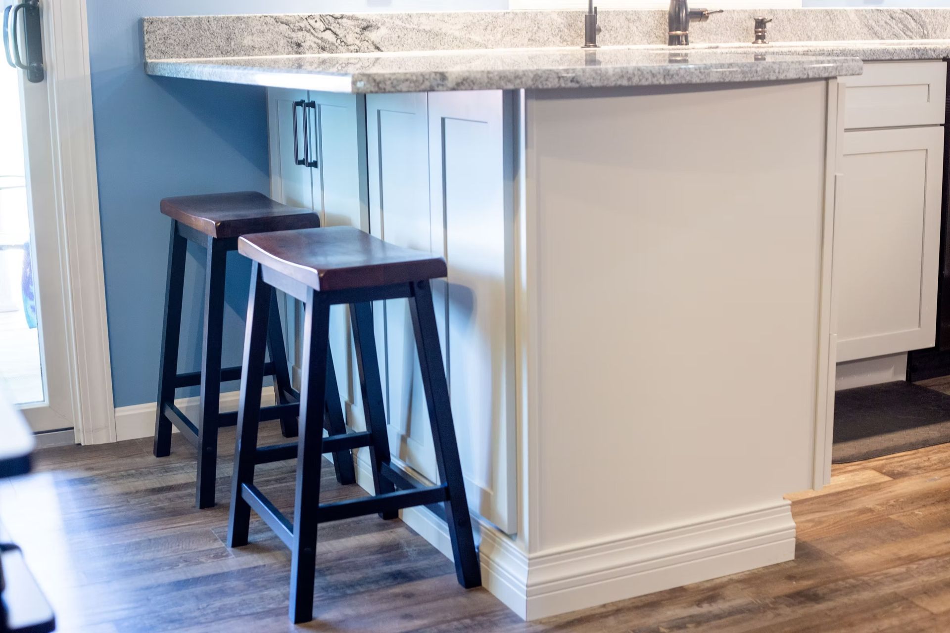 Two wooden bar stools at a white kitchen island with a granite countertop.