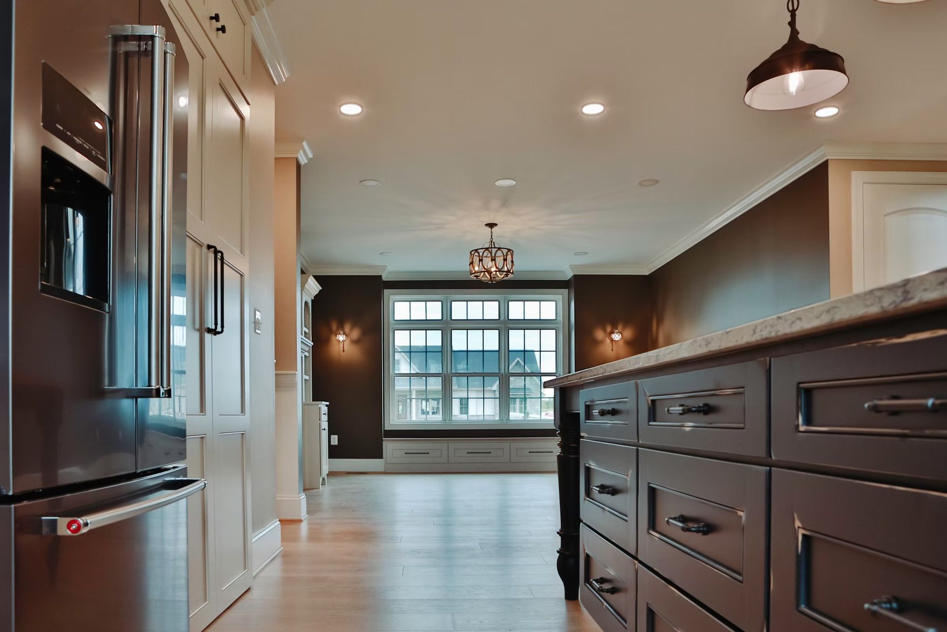 Modern kitchen with dark cabinets, stainless steel fridge, and a window at the end of the room.