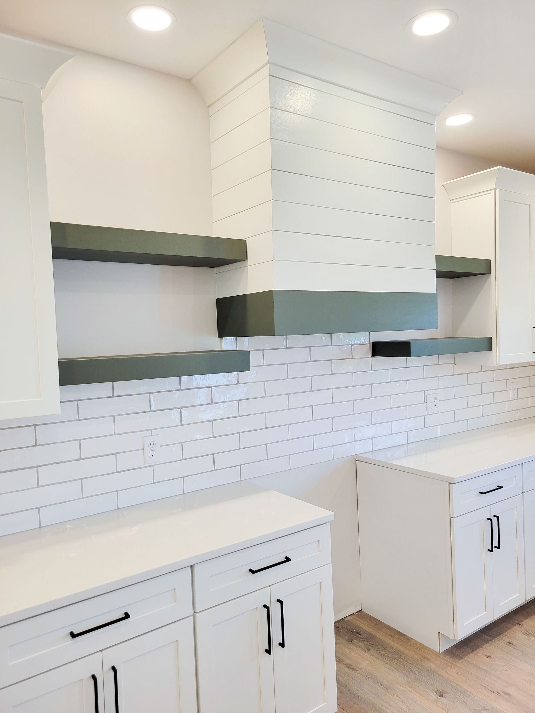 White kitchen with a brick backsplash, green shelves, and a range hood.