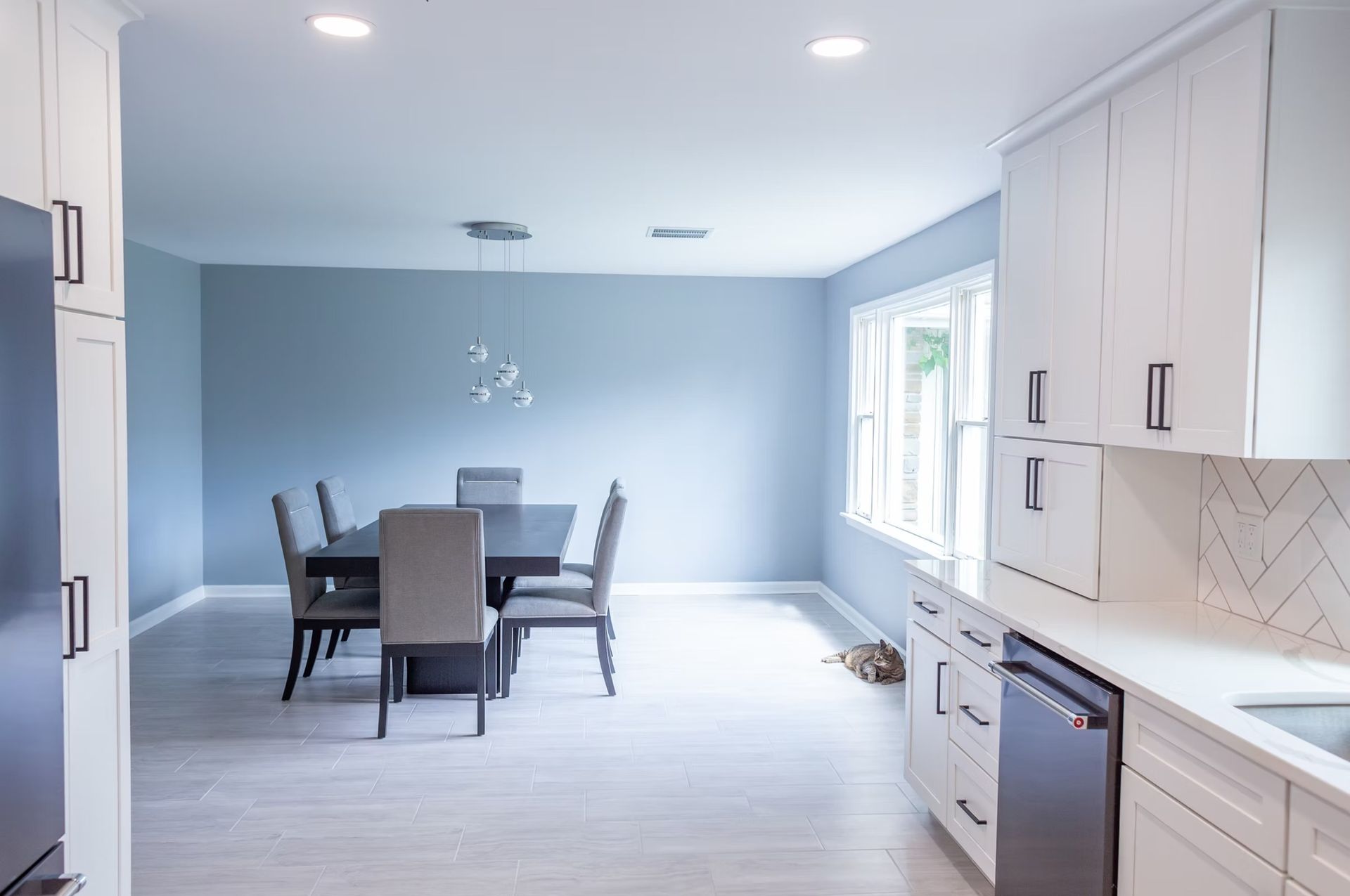Modern dining room with a table and chairs; light blue walls; white cabinets.