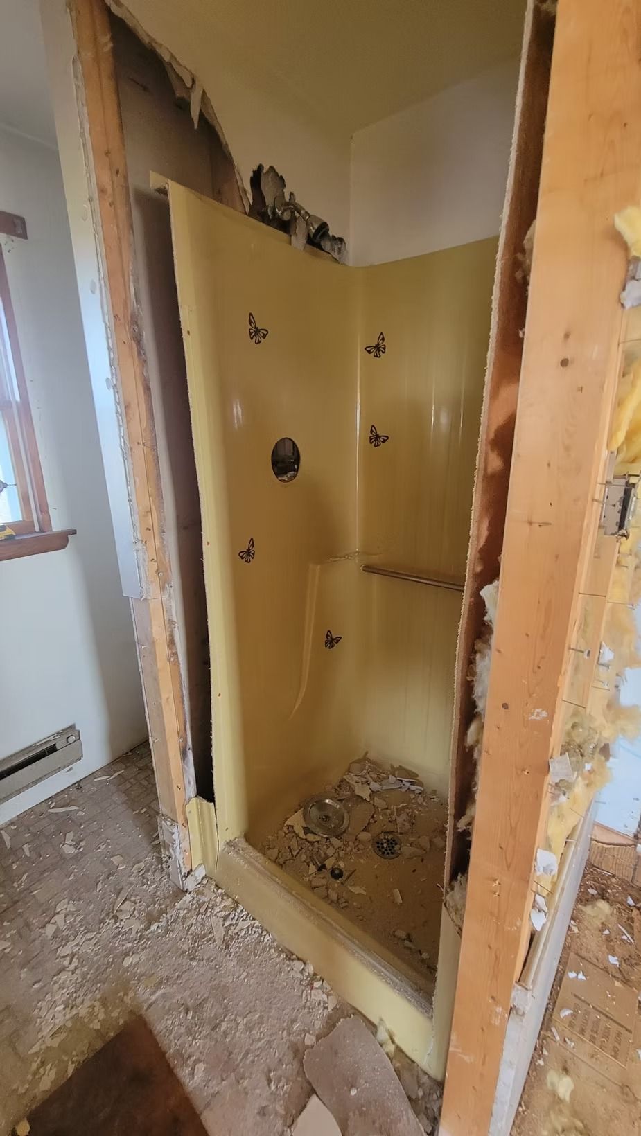 Yellow shower stall inside a partially demolished bathroom.