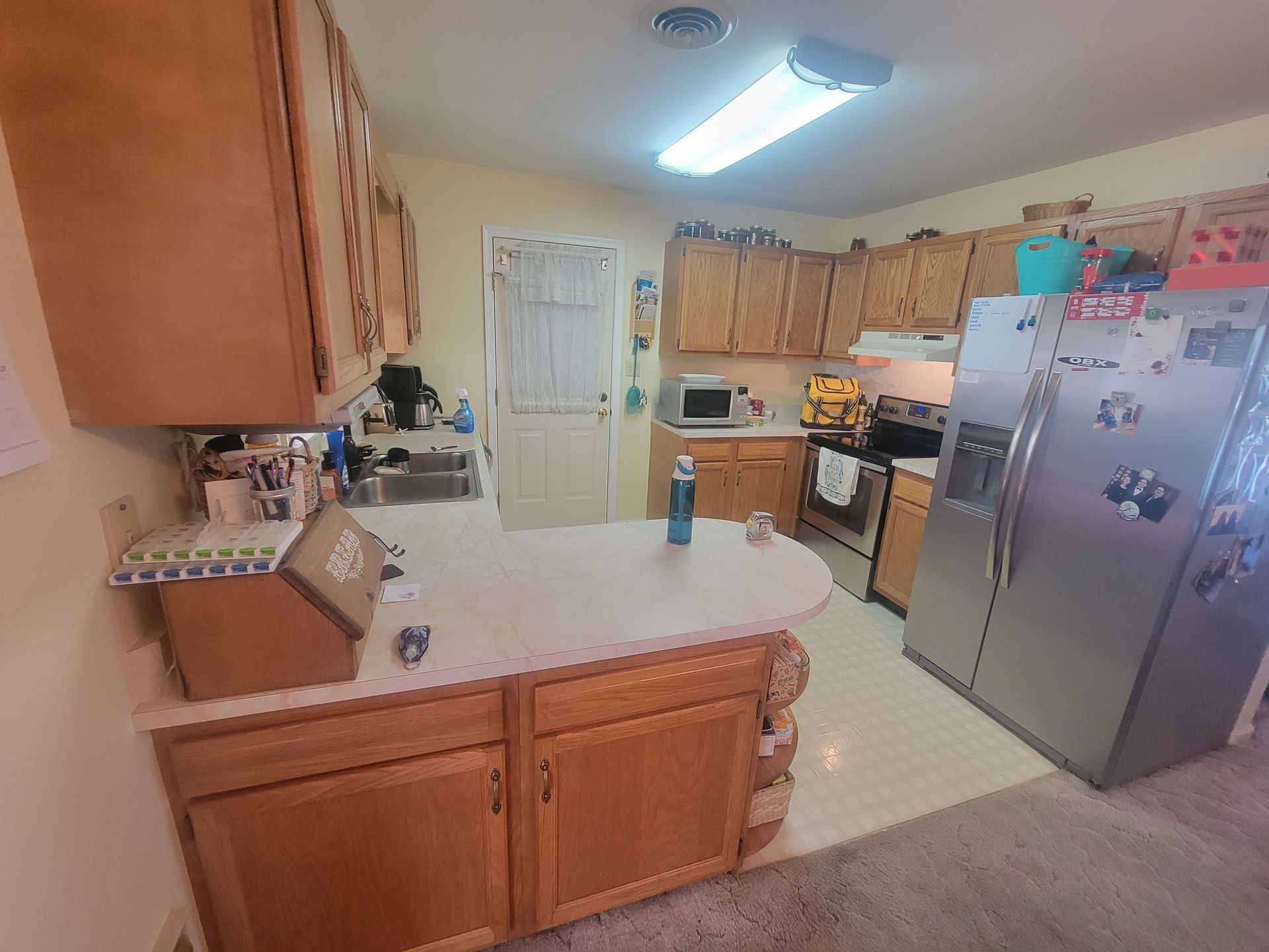 Kitchen with wood cabinets, white countertops, stainless steel refrigerator, and a door.