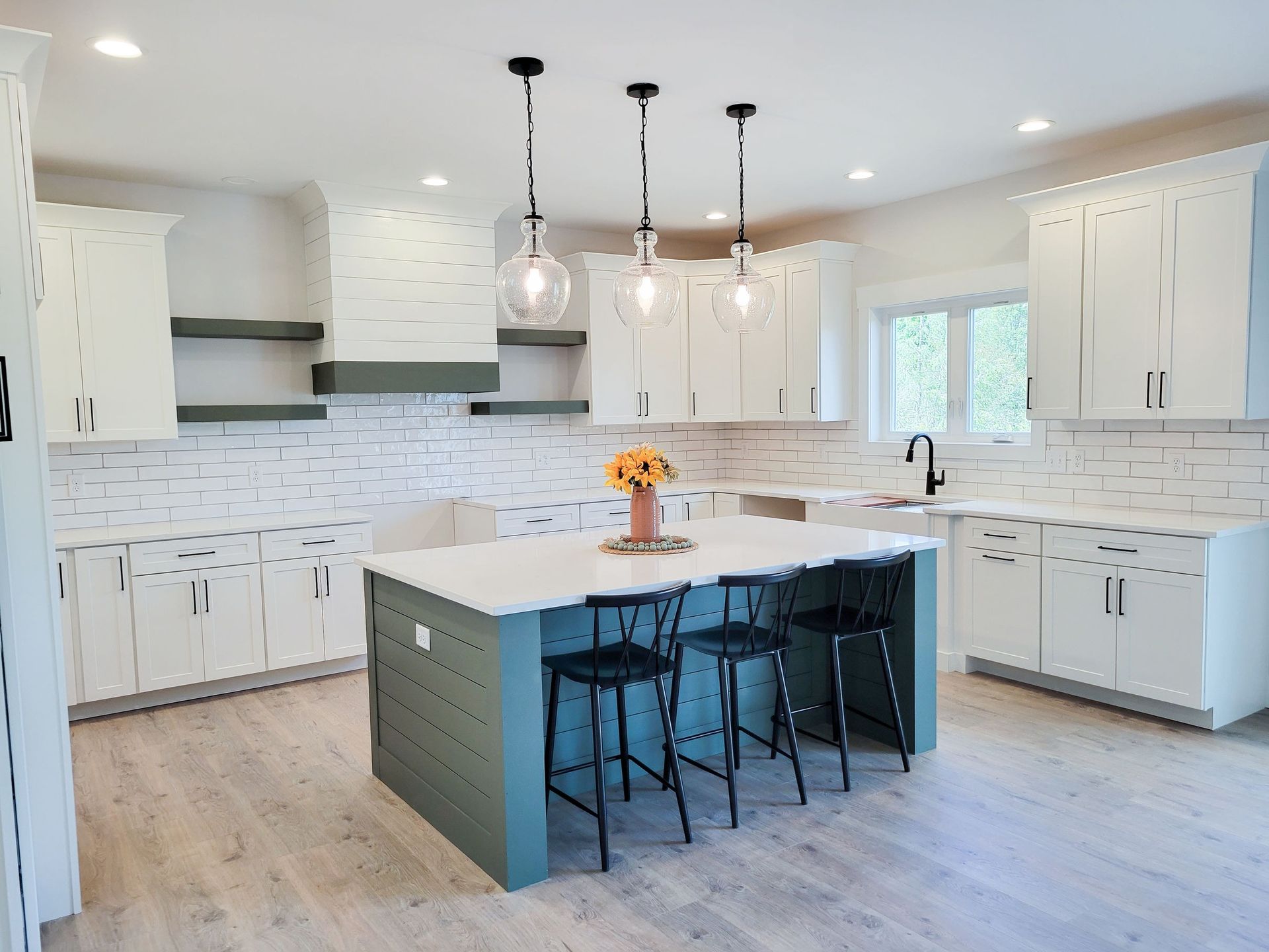 Modern kitchen with white cabinets, teal island with black stools, and pendant lights.
