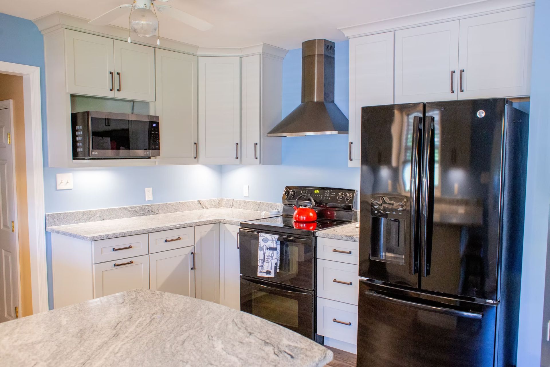 A bright, updated kitchen featuring white cabinets, black appliances, and a granite countertop.