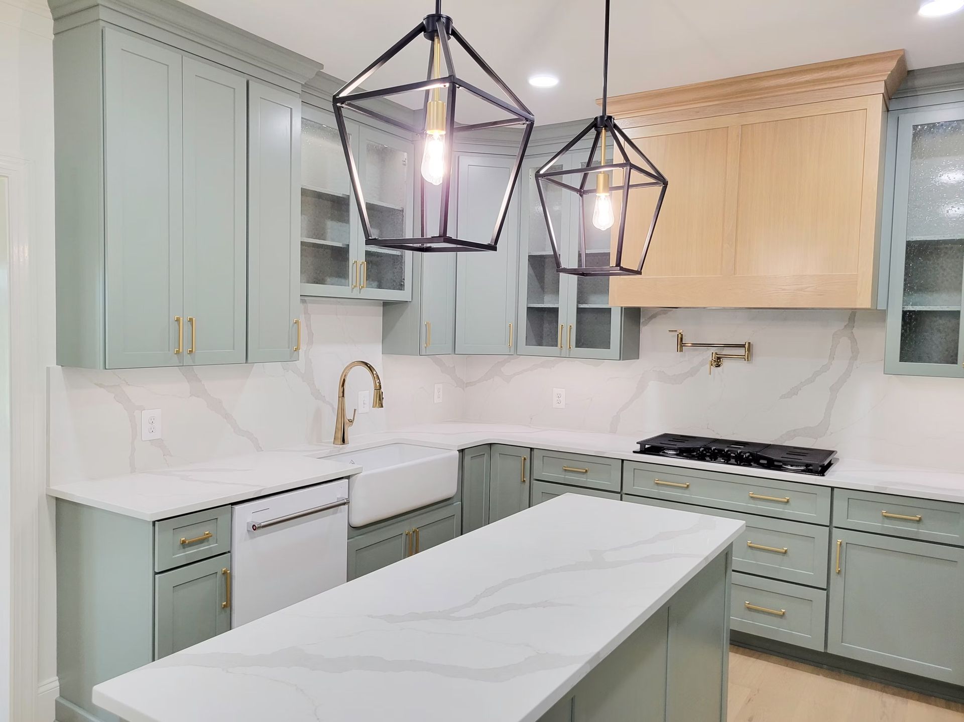 Green kitchen with white countertops, island, and modern black geometric light fixtures.