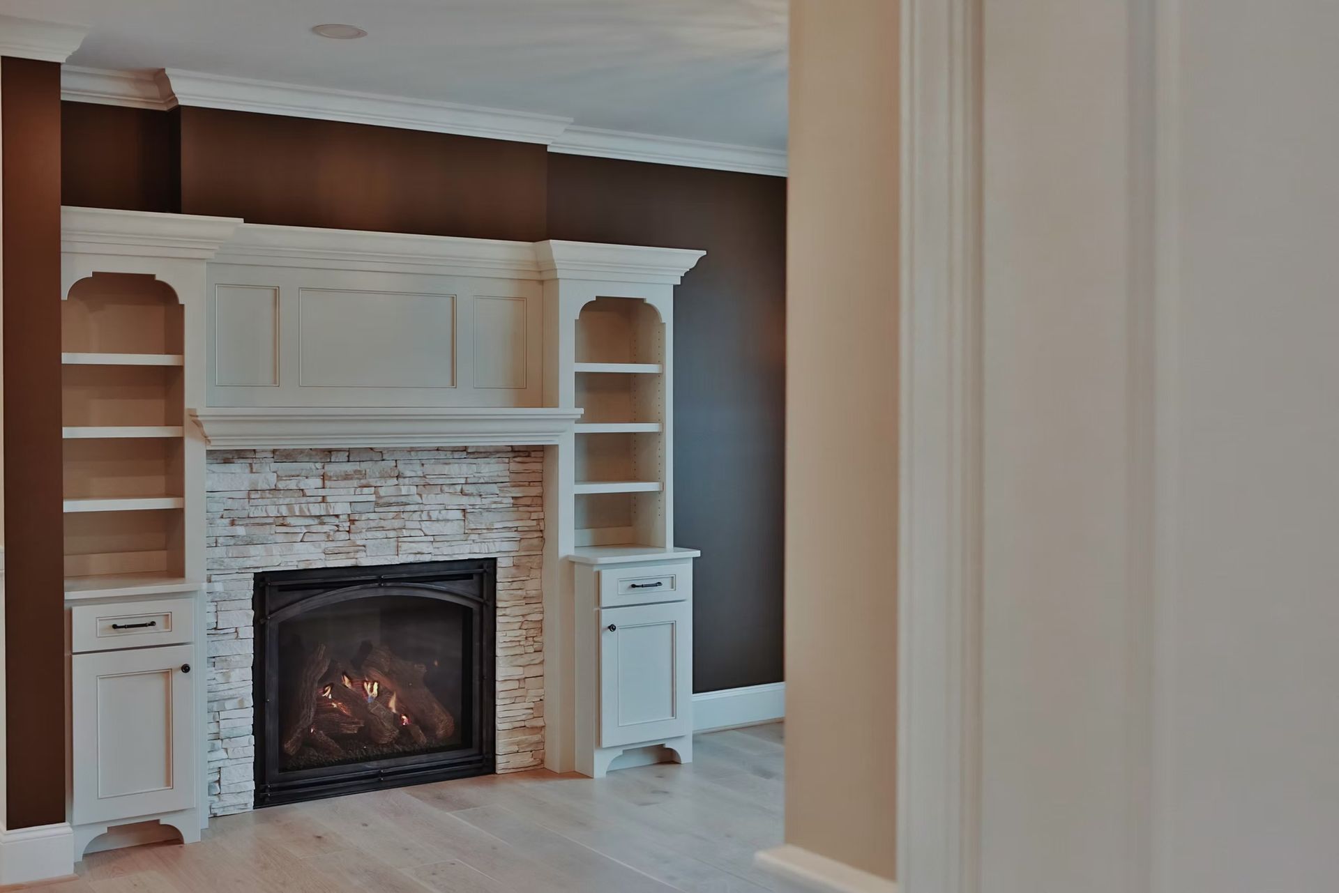 Fireplace with built-in shelves and cabinets; white stonework, dark brown wall, and light wood floor.