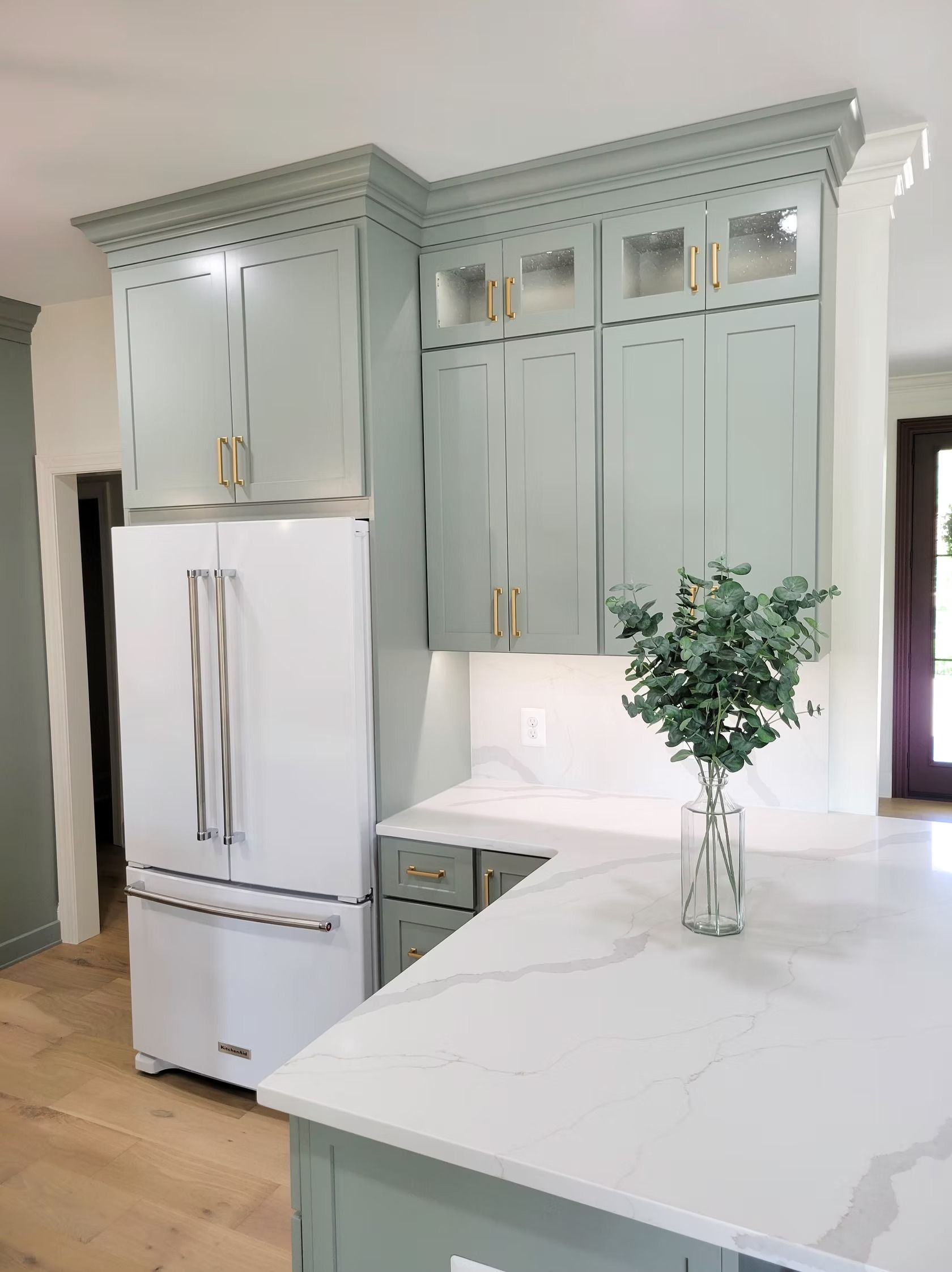 Blue-green kitchen cabinets with a white refrigerator, gold hardware, and a white countertop.