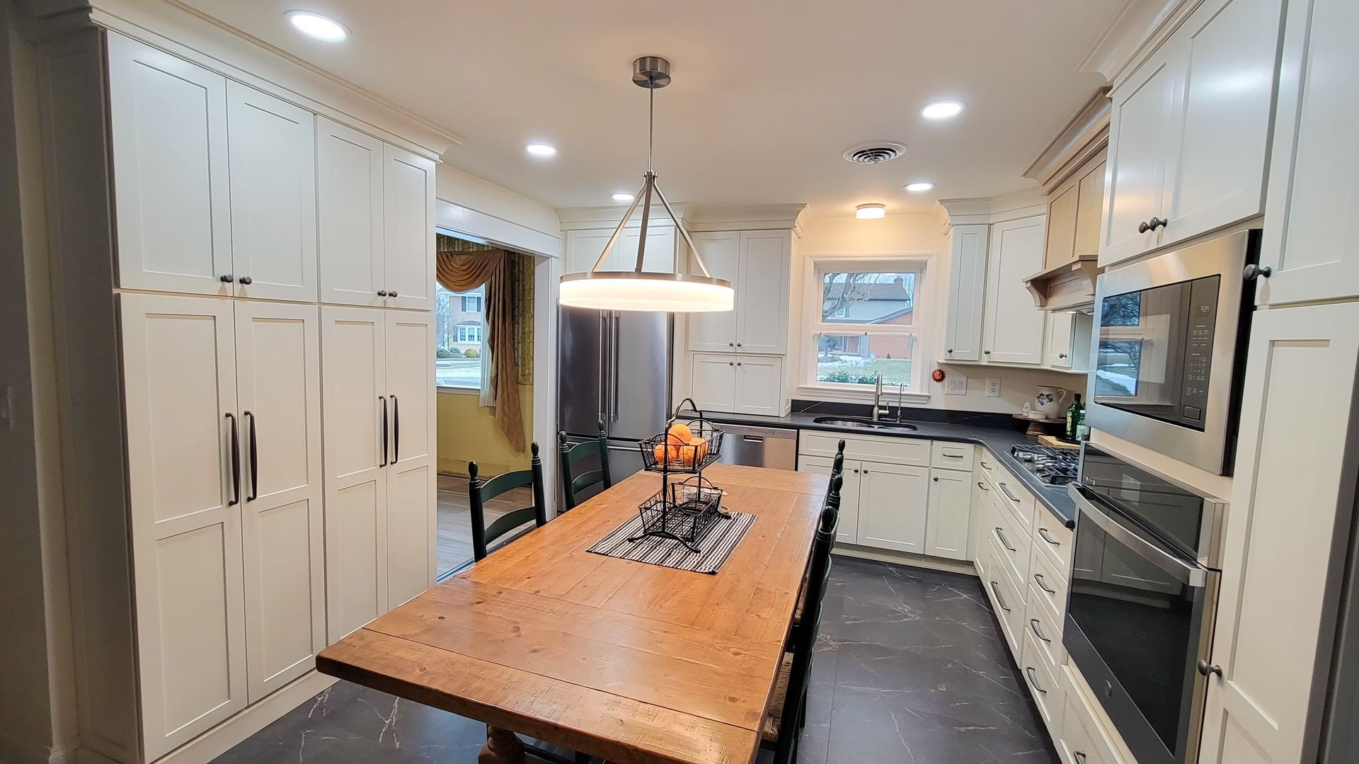 Cream-colored kitchen with a wooden table, cabinets, and a window; a stove and a microwave.