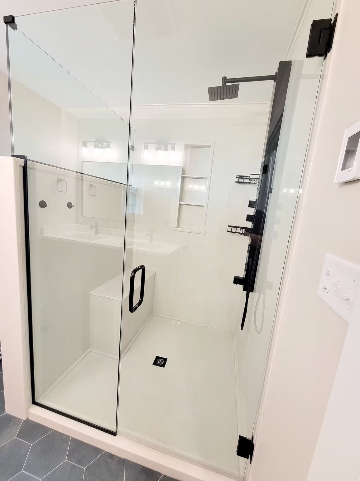 Glass-walled shower with black fixtures and a built-in seat, in a white bathroom.