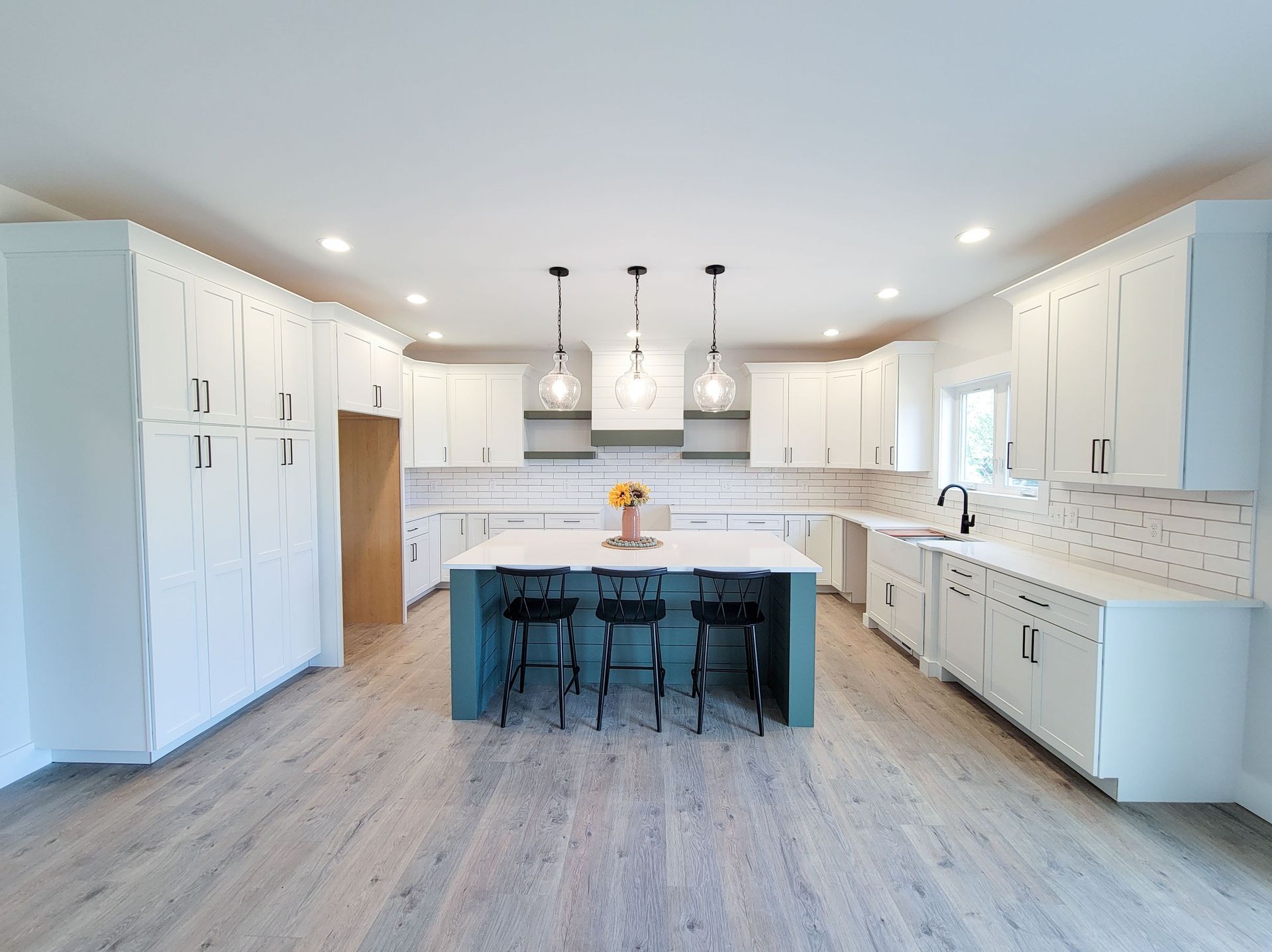 Spacious white kitchen with blue island, three pendant lights, and light wood floors.