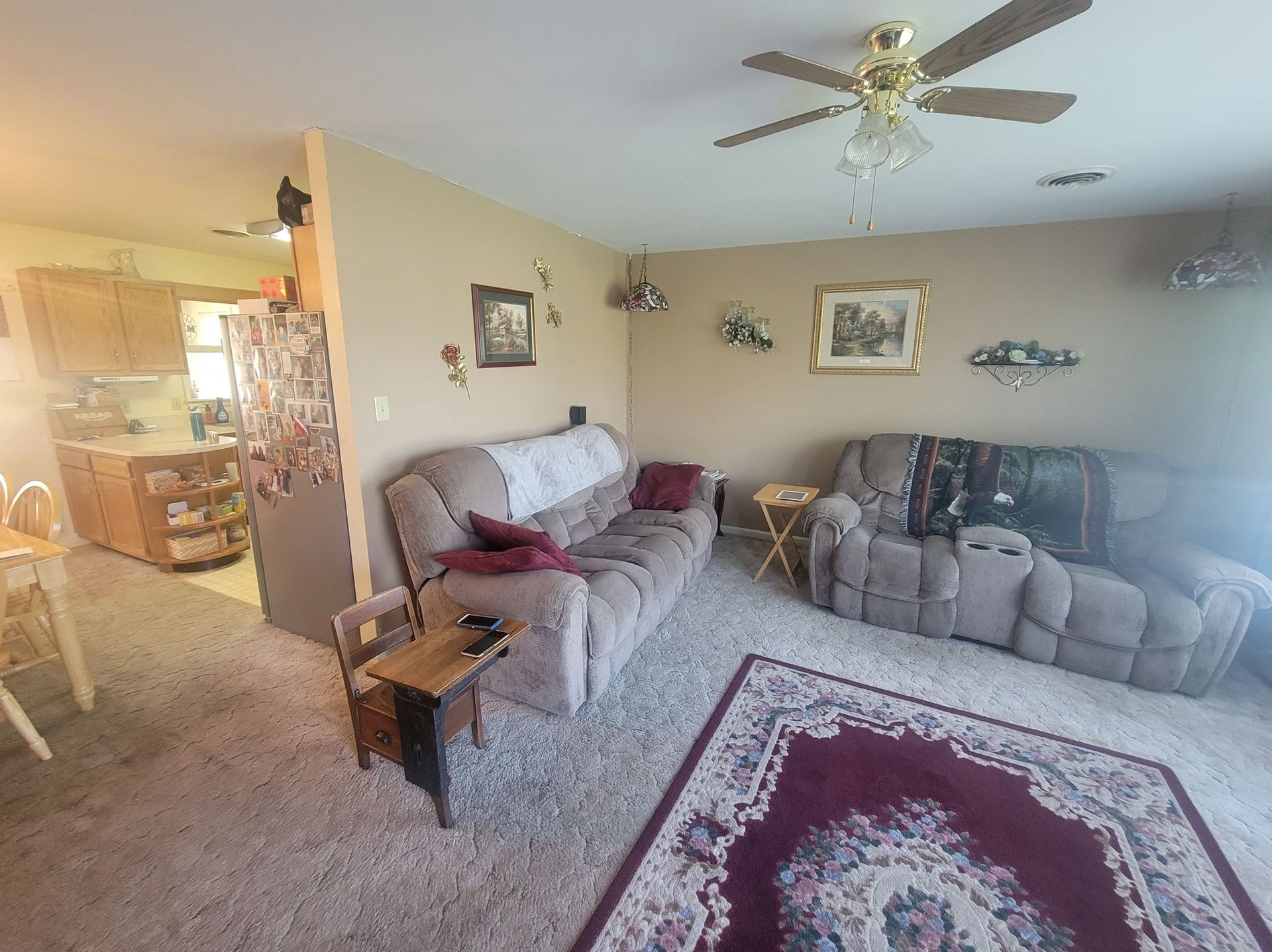 Cozy living room with tan walls, brown furniture, and a red rug. View into the kitchen.