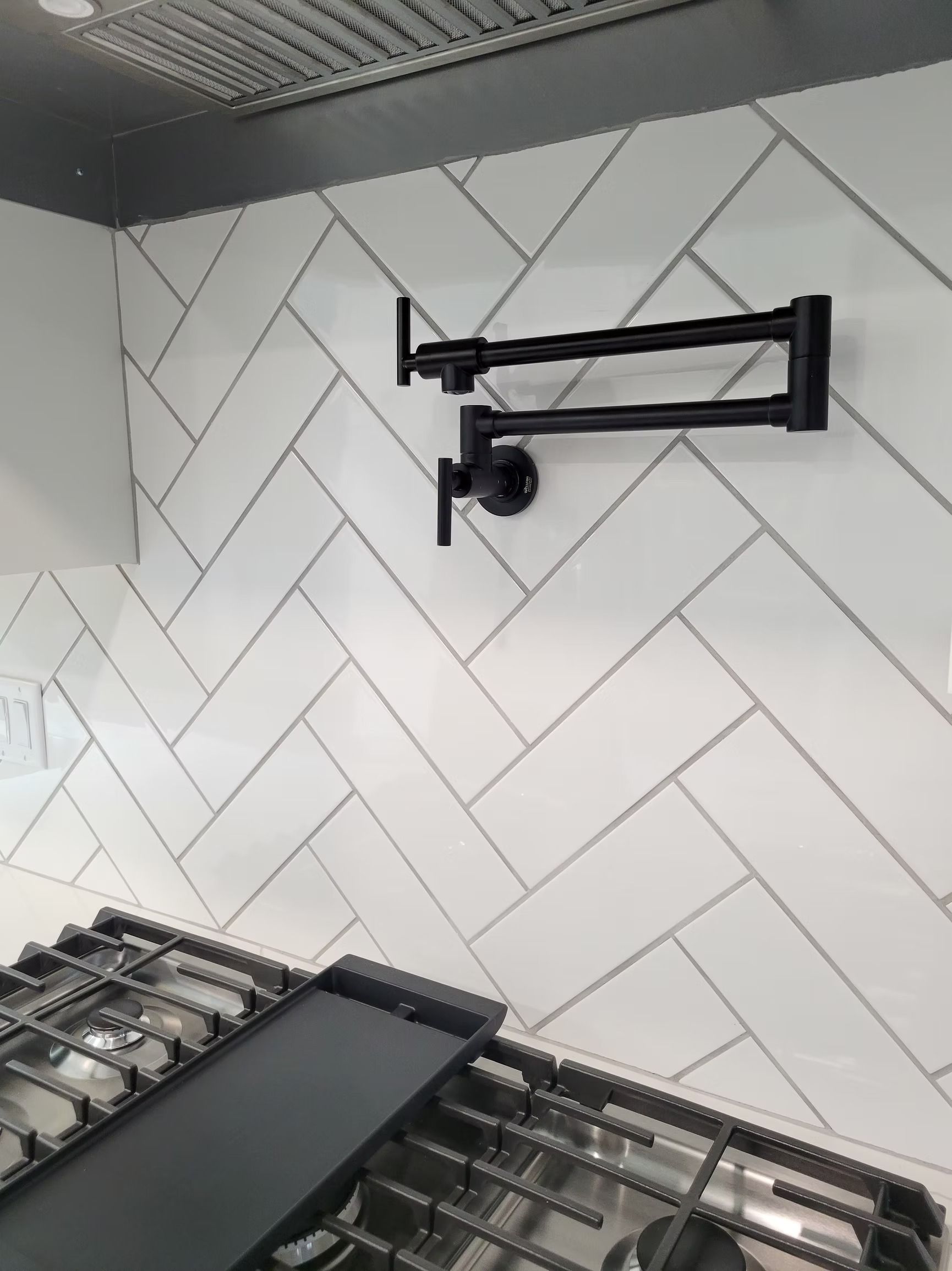 Black pot filler over a gas stovetop against a white herringbone tiled backsplash.