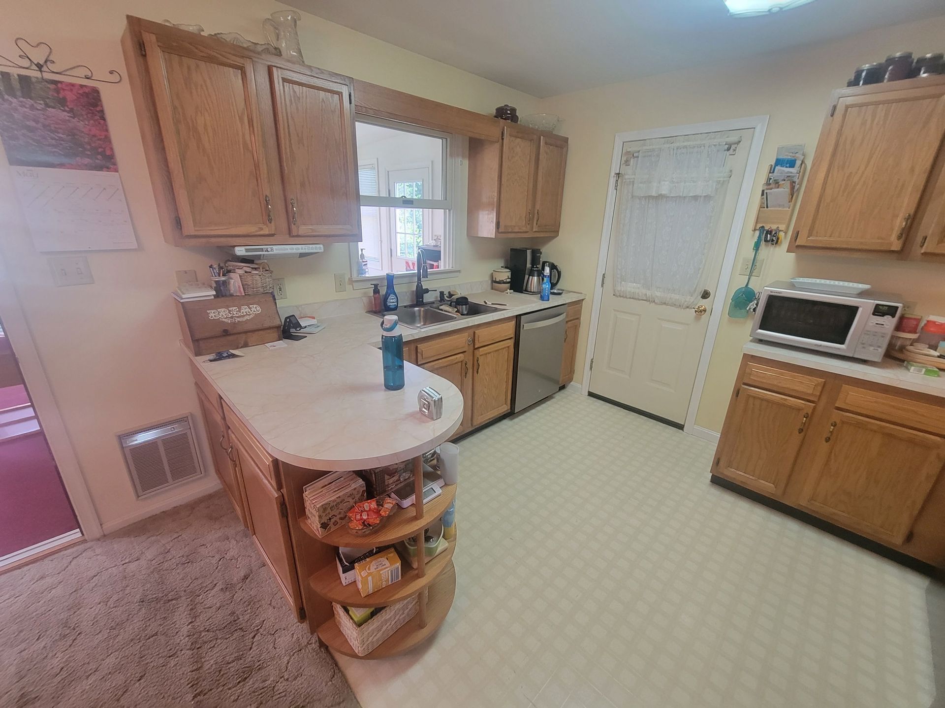 Kitchen with light cabinets, white countertops, appliances, and a door.