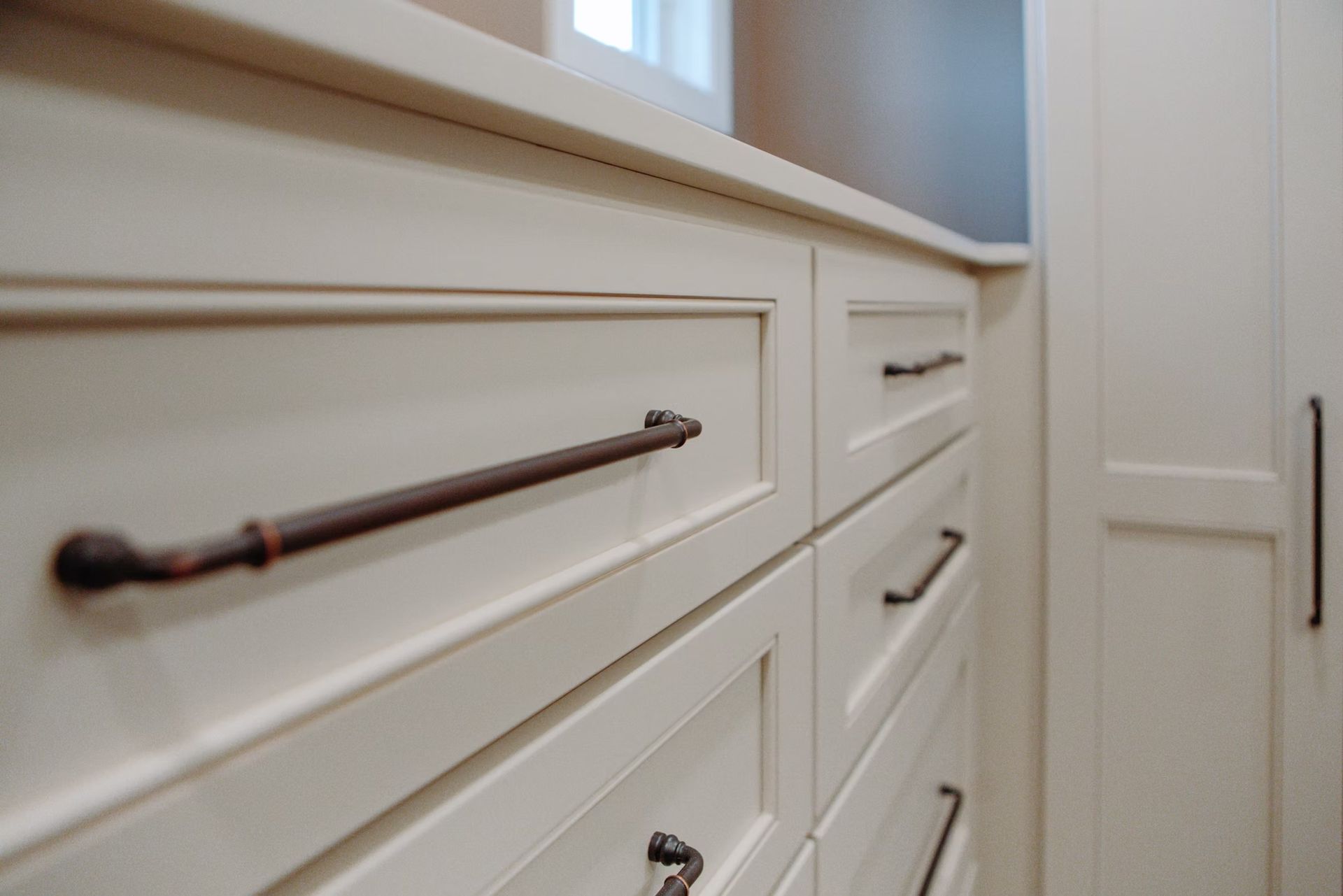 Cream-colored cabinets with dark bronze handles in a bright, clean room.