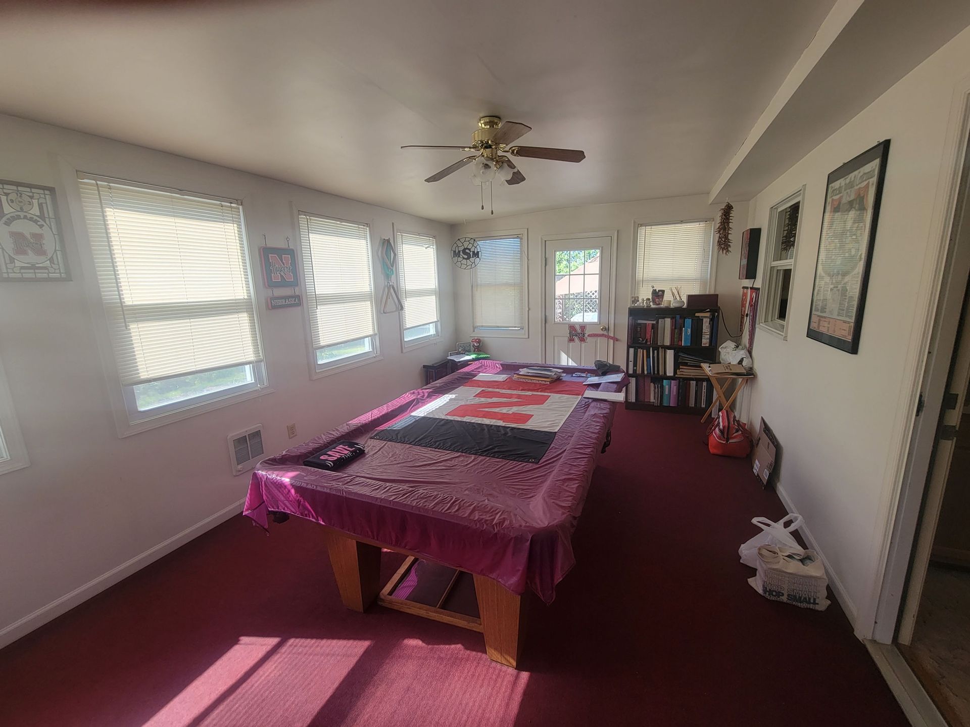Pool table in a room with red carpet, windows, and a bookshelf.