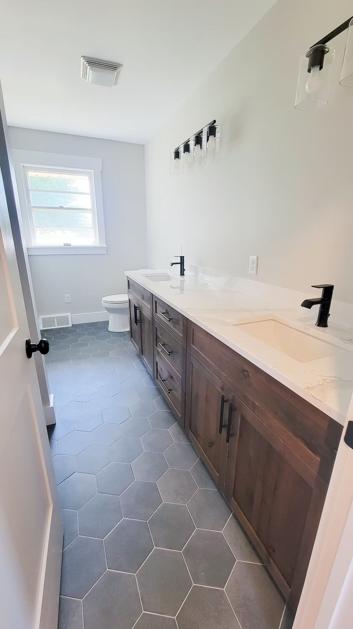Bathroom with dark wood vanity, white countertop, black fixtures, and patterned gray floor.