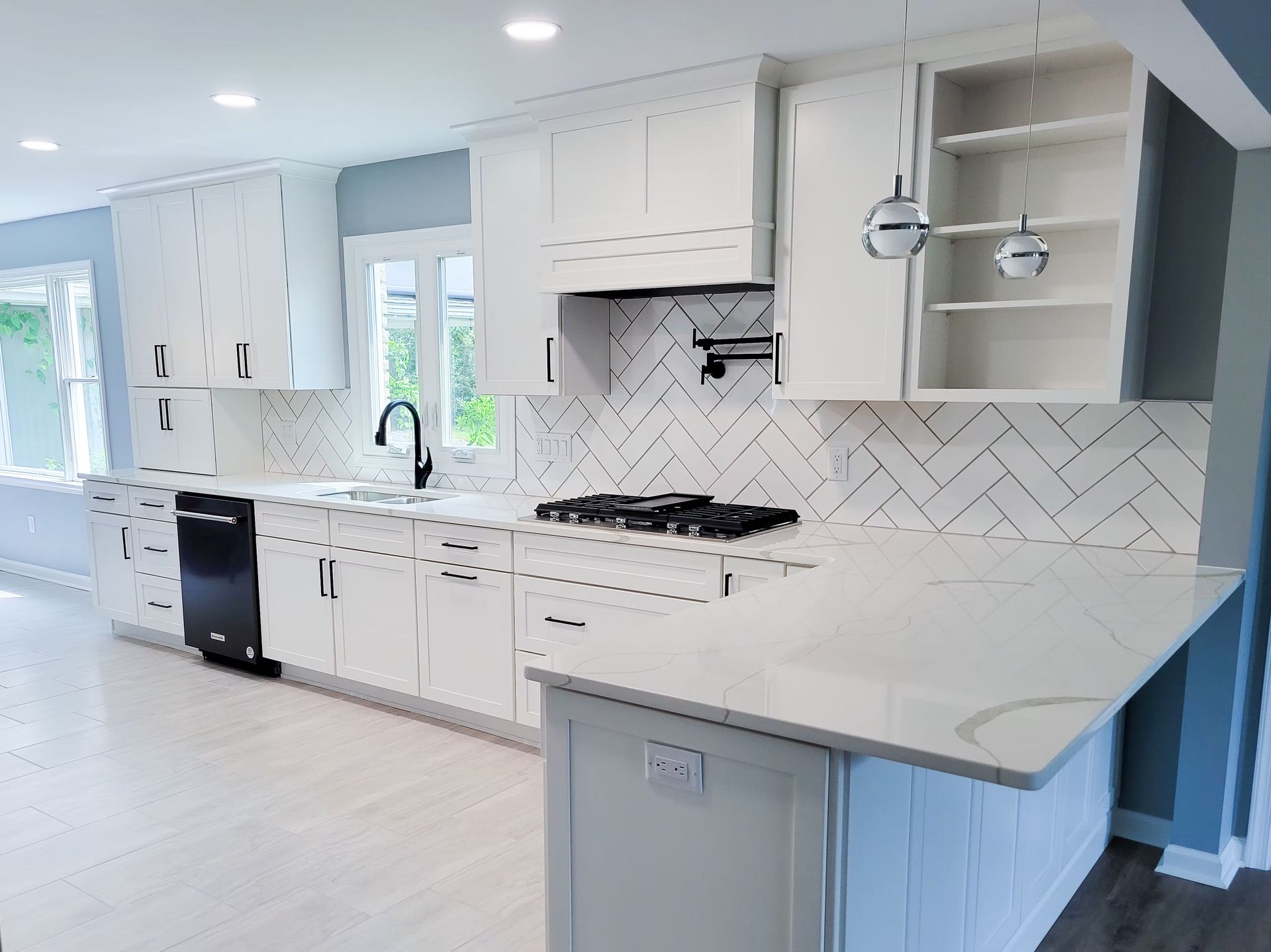 Modern white kitchen with black appliances, backsplash, and faucet.