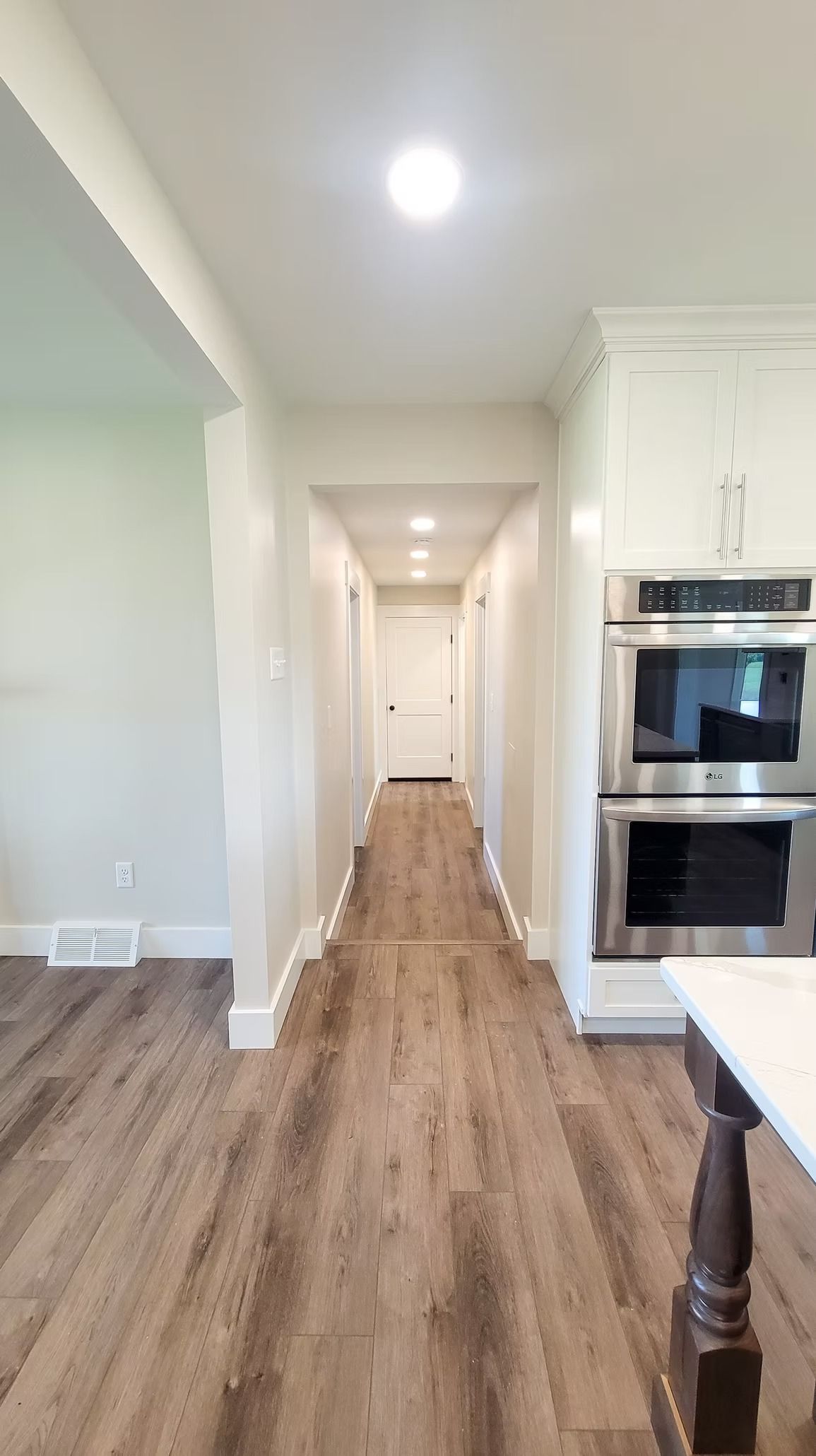 Hallway with light-colored walls, wood-look floor, and built-in double oven.