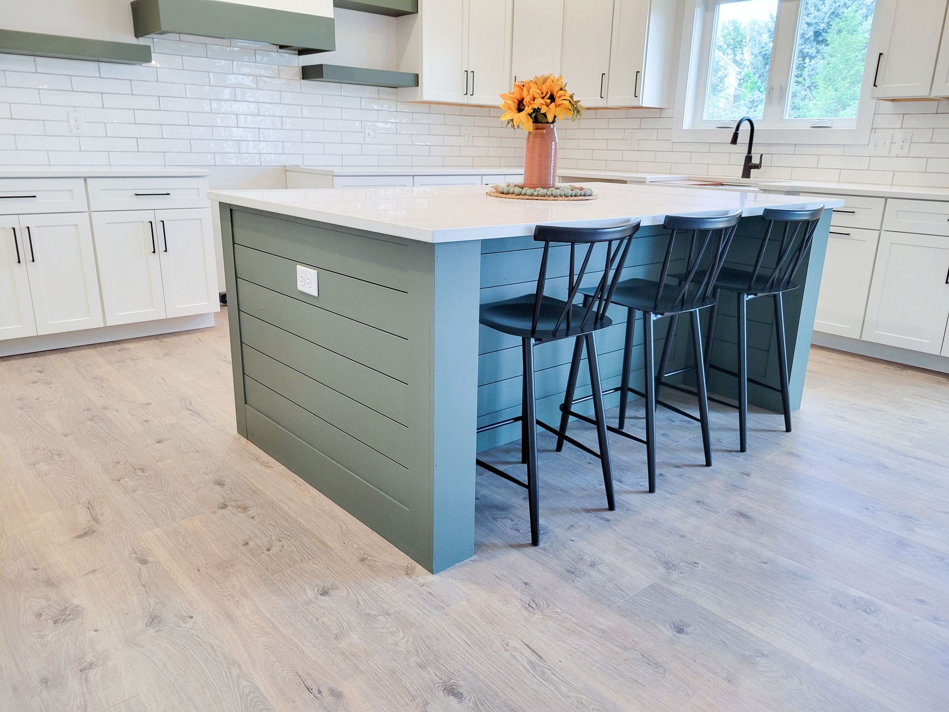 Kitchen with a sage green island, white countertops, and black bar stools.