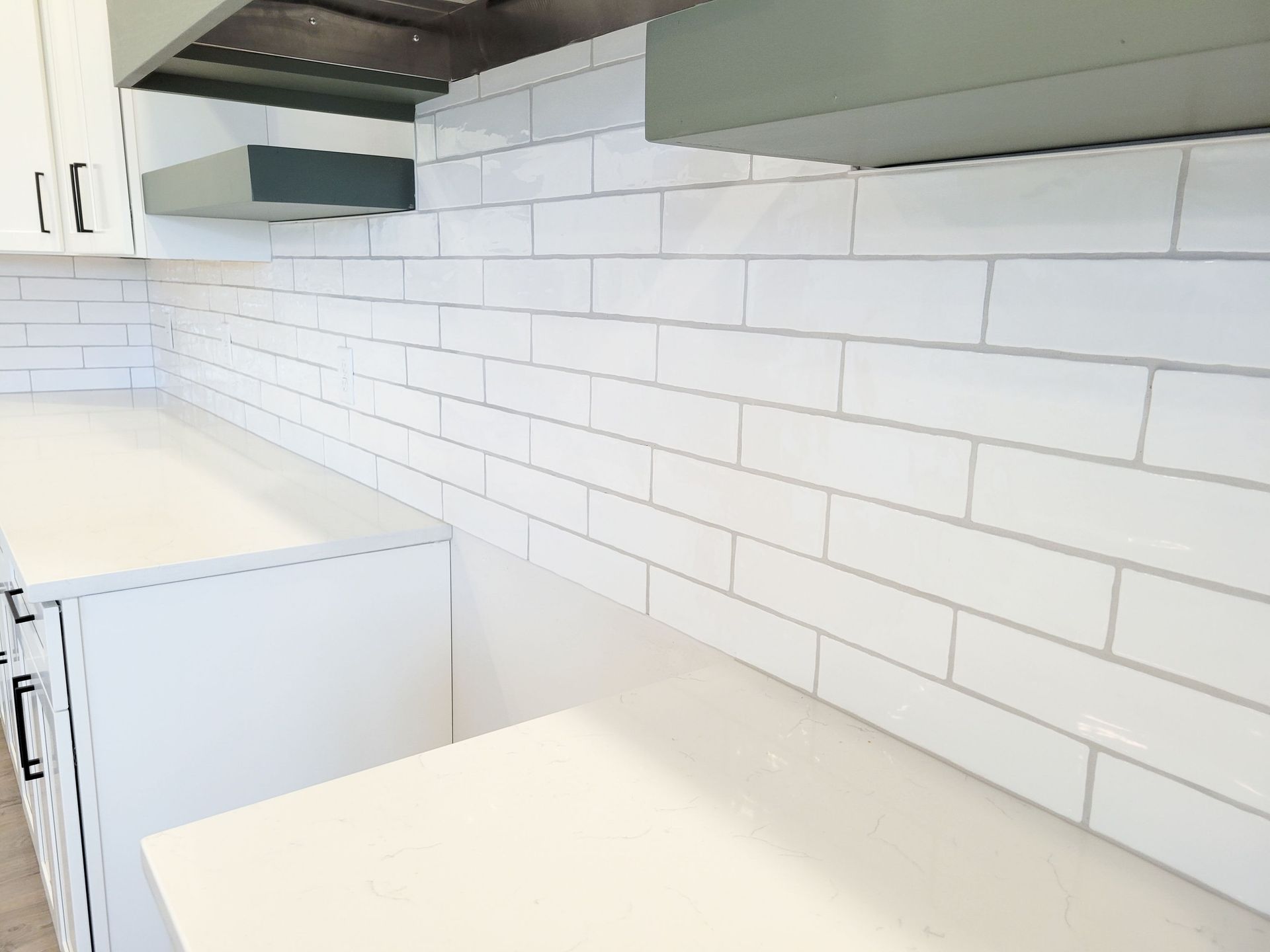 White kitchen with white subway tile backsplash, white counters, and green range hood.