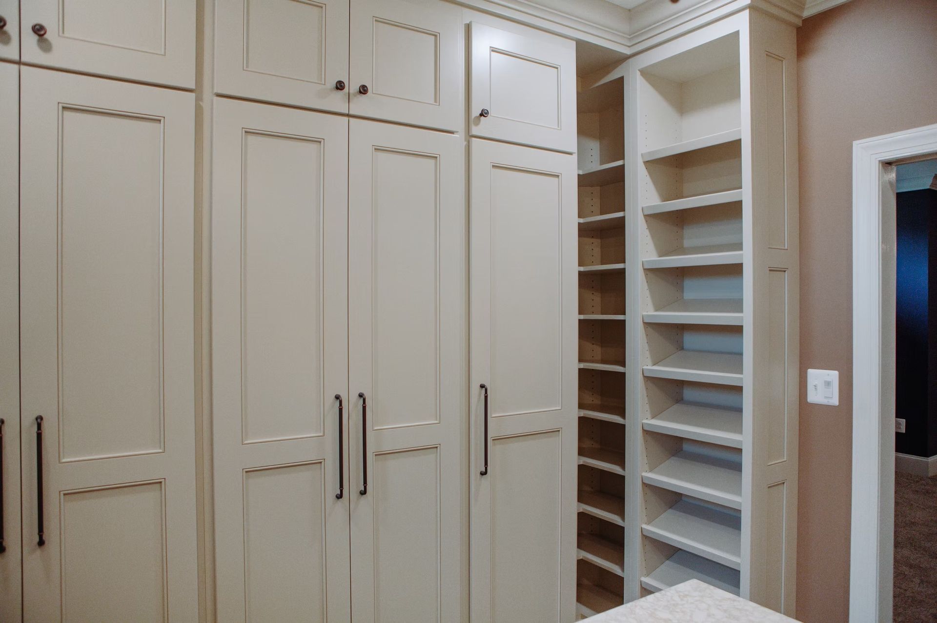 Cream-colored built-in cabinets and shelving in a room, with a partially visible door and a decorative ceiling detail.