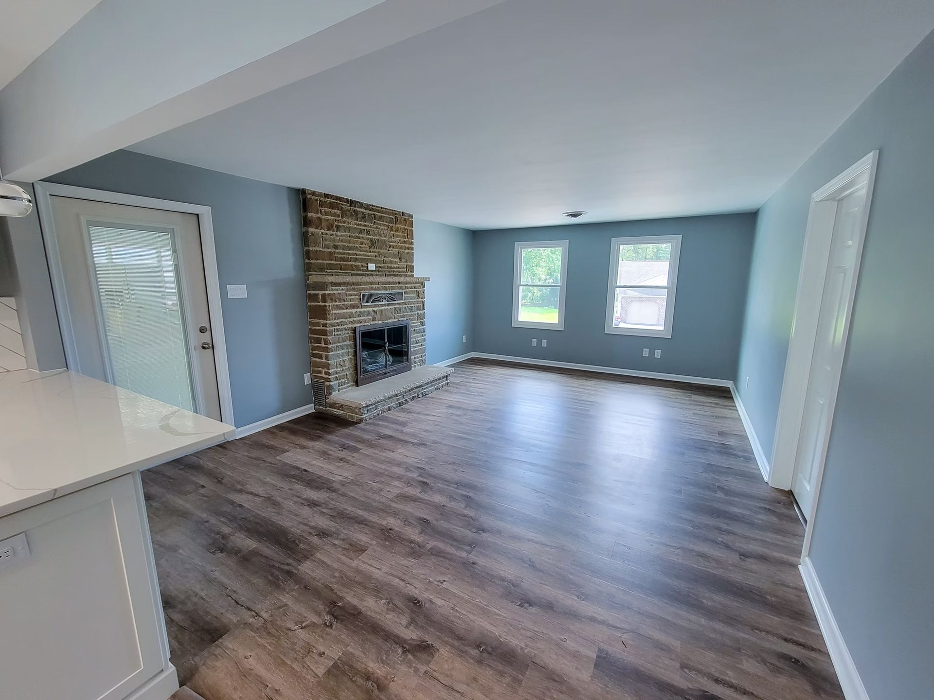 Living room with gray walls, brick fireplace, wood floors, and two windows.