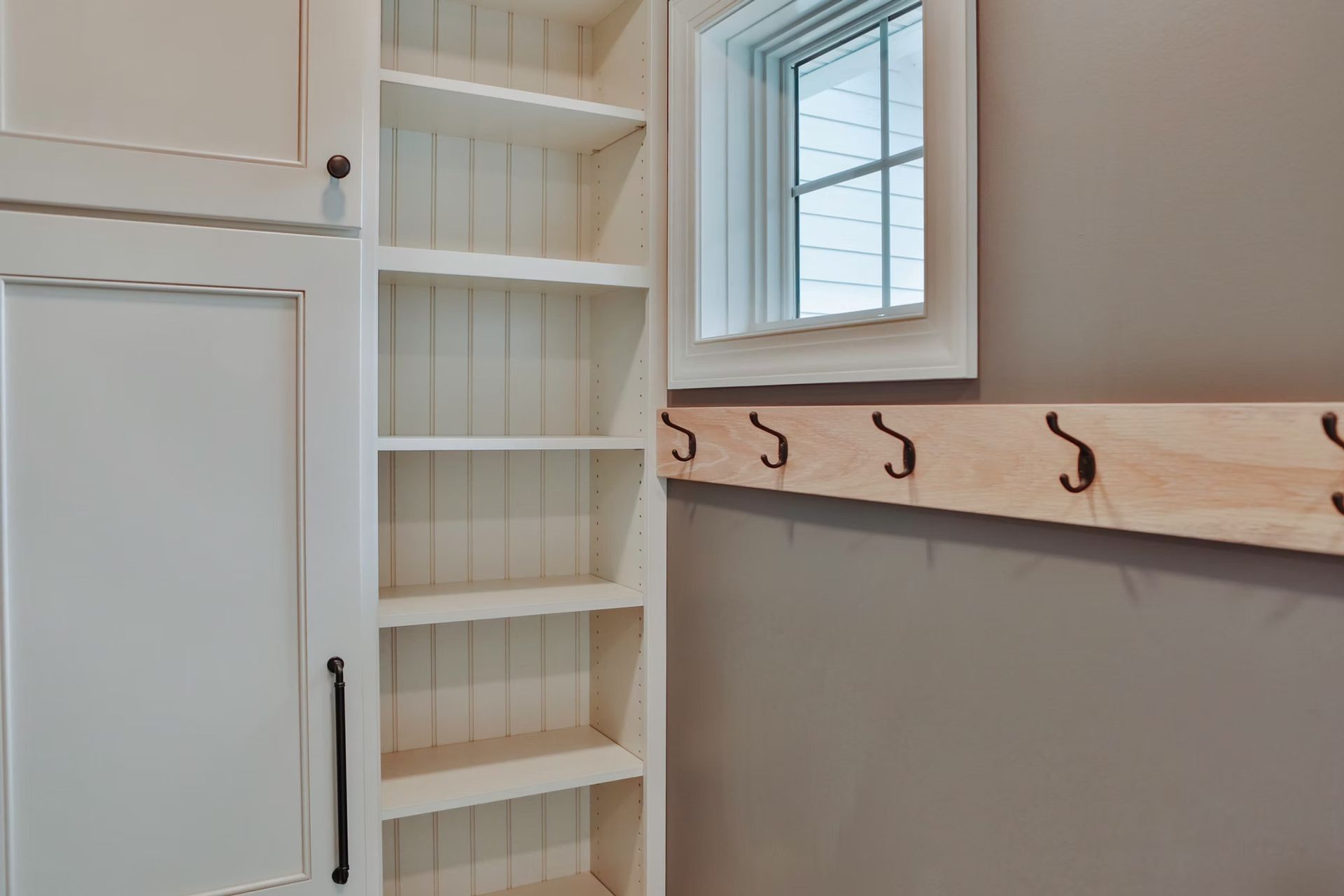 Built-in white shelving and cabinet next to a wooden coat rack and a small window.