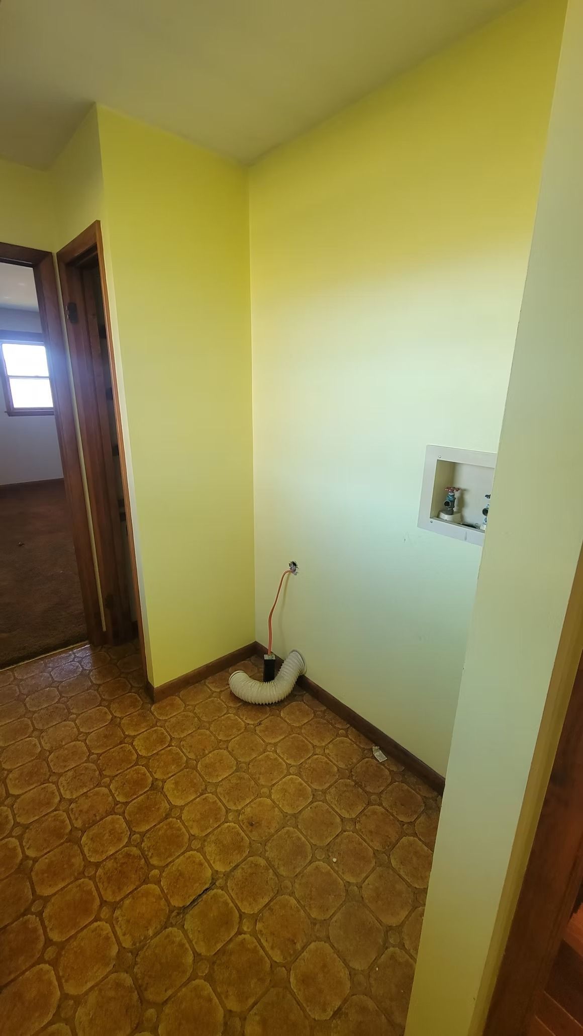 Yellow laundry room with washing machine hookups, brown flooring and doorway to a hallway.