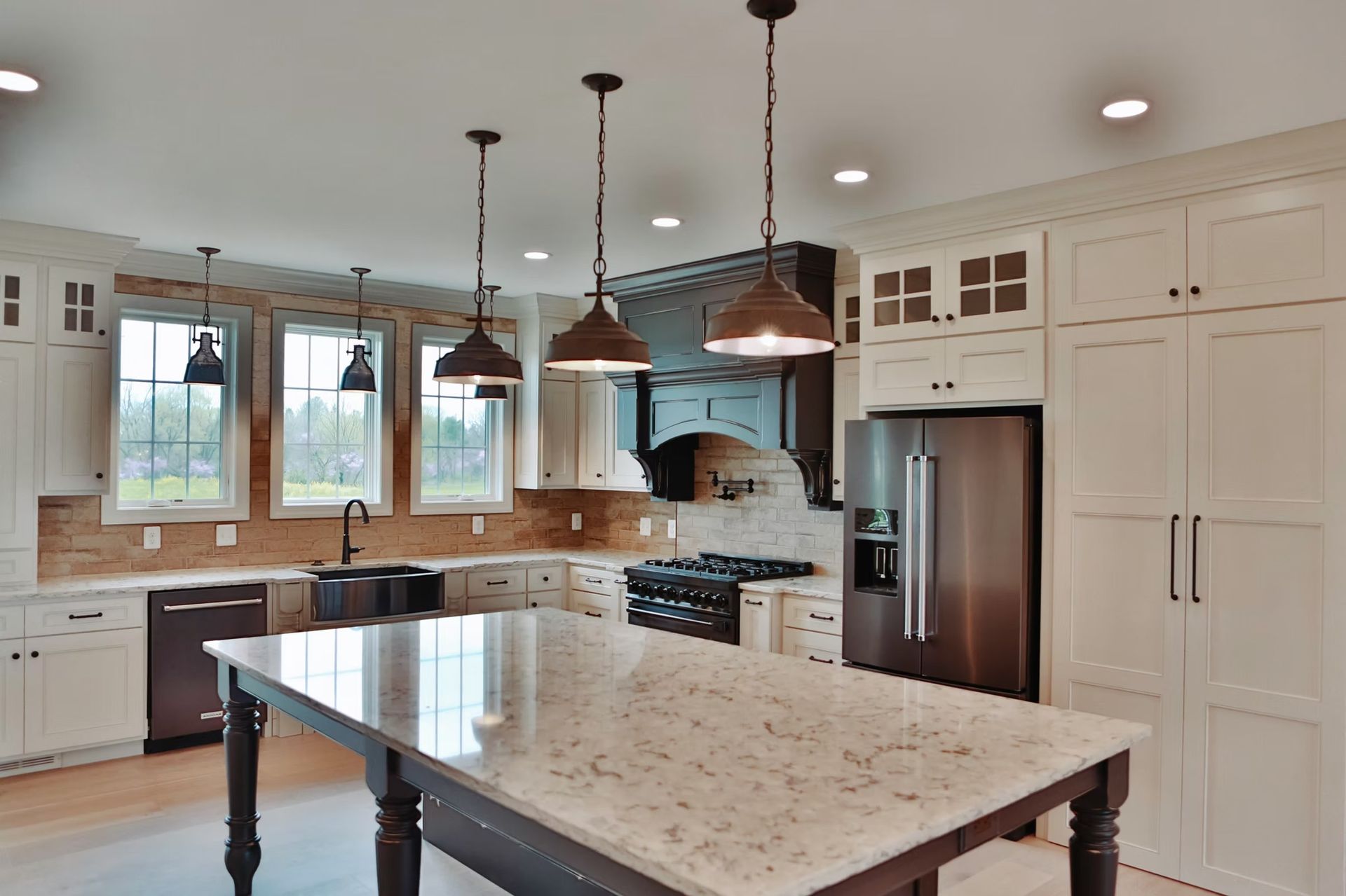 Spacious kitchen with white cabinets, large island, black appliances, and pendant lights.