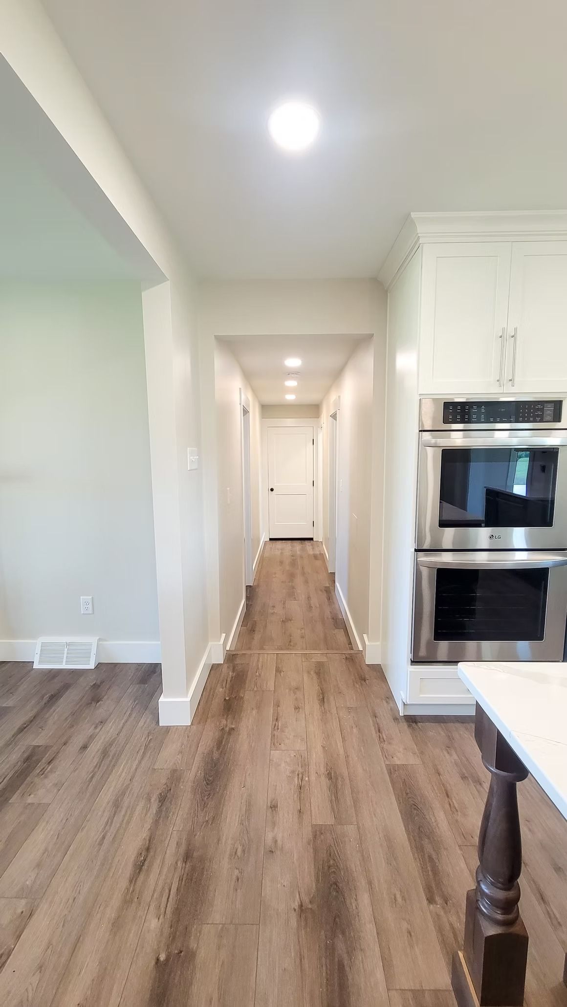 Narrow kitchen hallway with wooden floor, white walls, and built-in ovens.