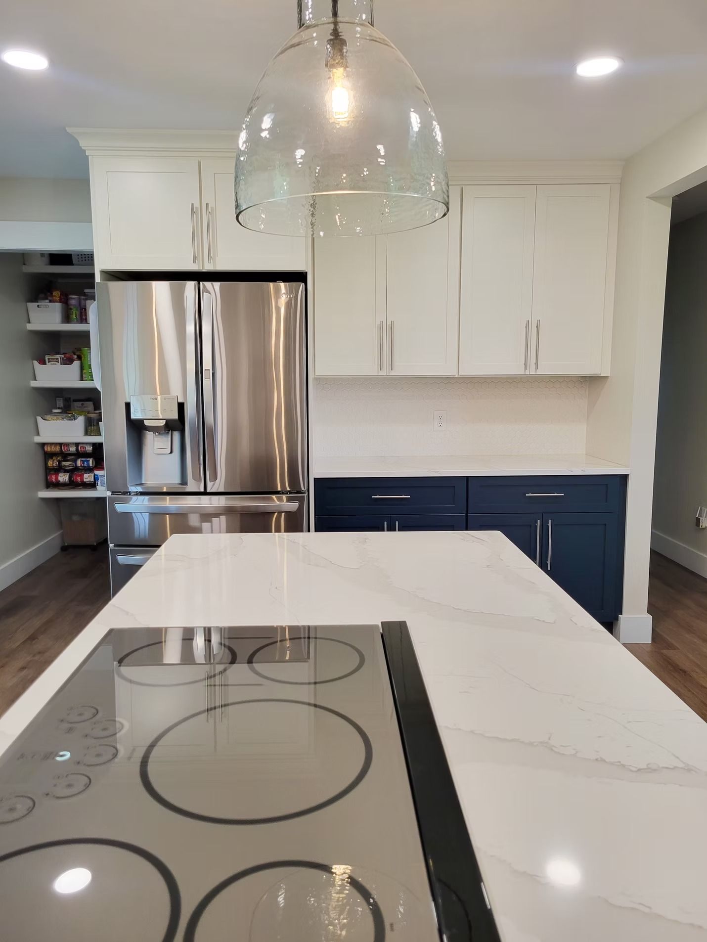 Modern kitchen with white and blue cabinets, stainless steel appliances, and an island with a stovetop.