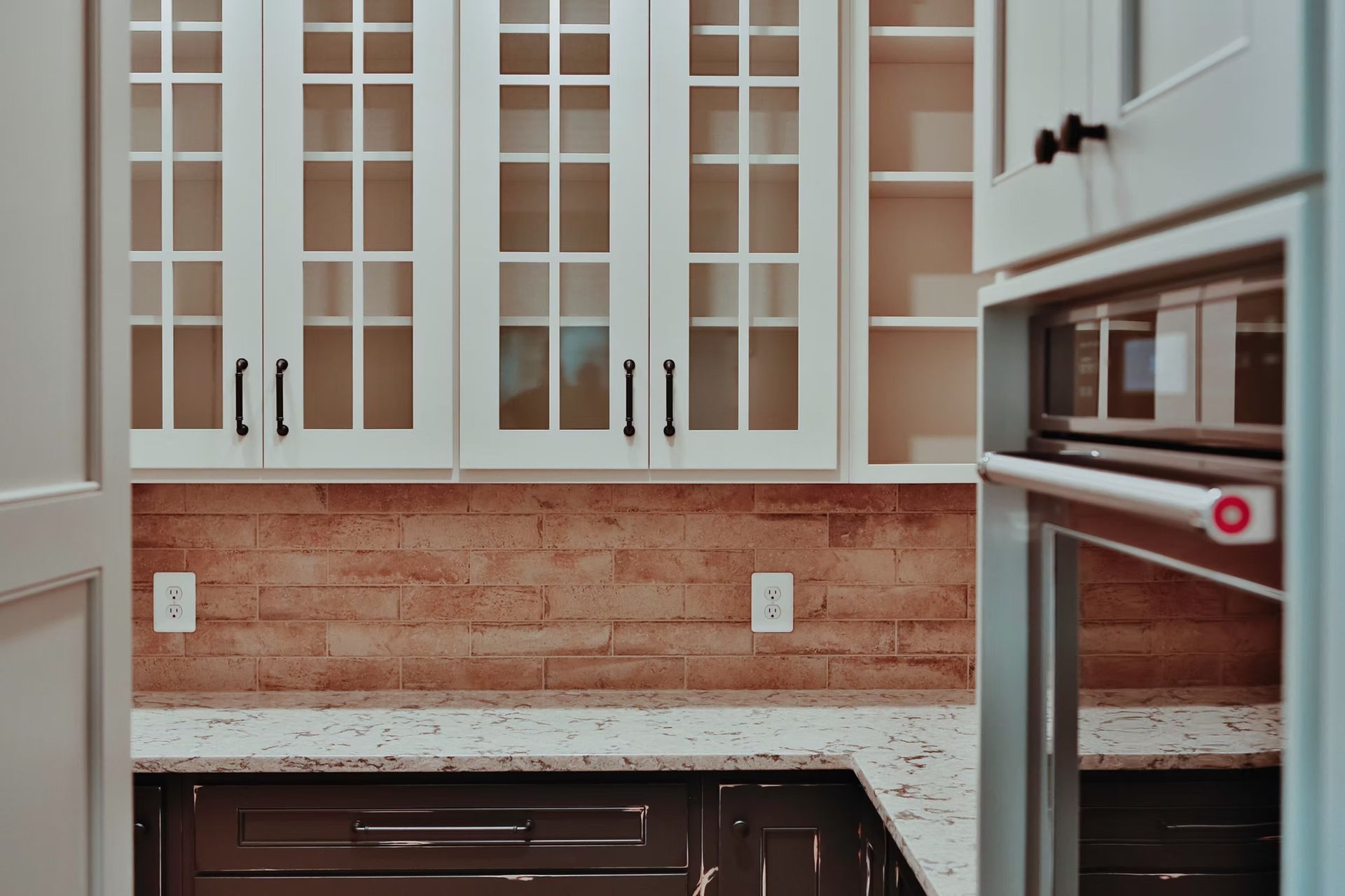 Kitchen cabinets with glass doors above a backsplash, and a built-in oven.