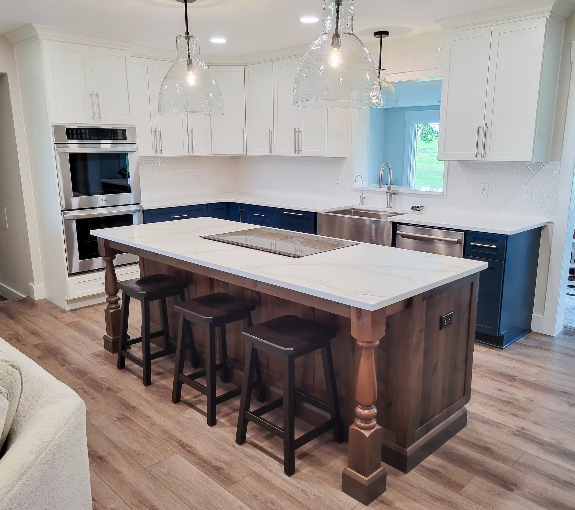 A modern kitchen with white cabinets, a blue island, and wood floors. Includes seating and pendant lights.