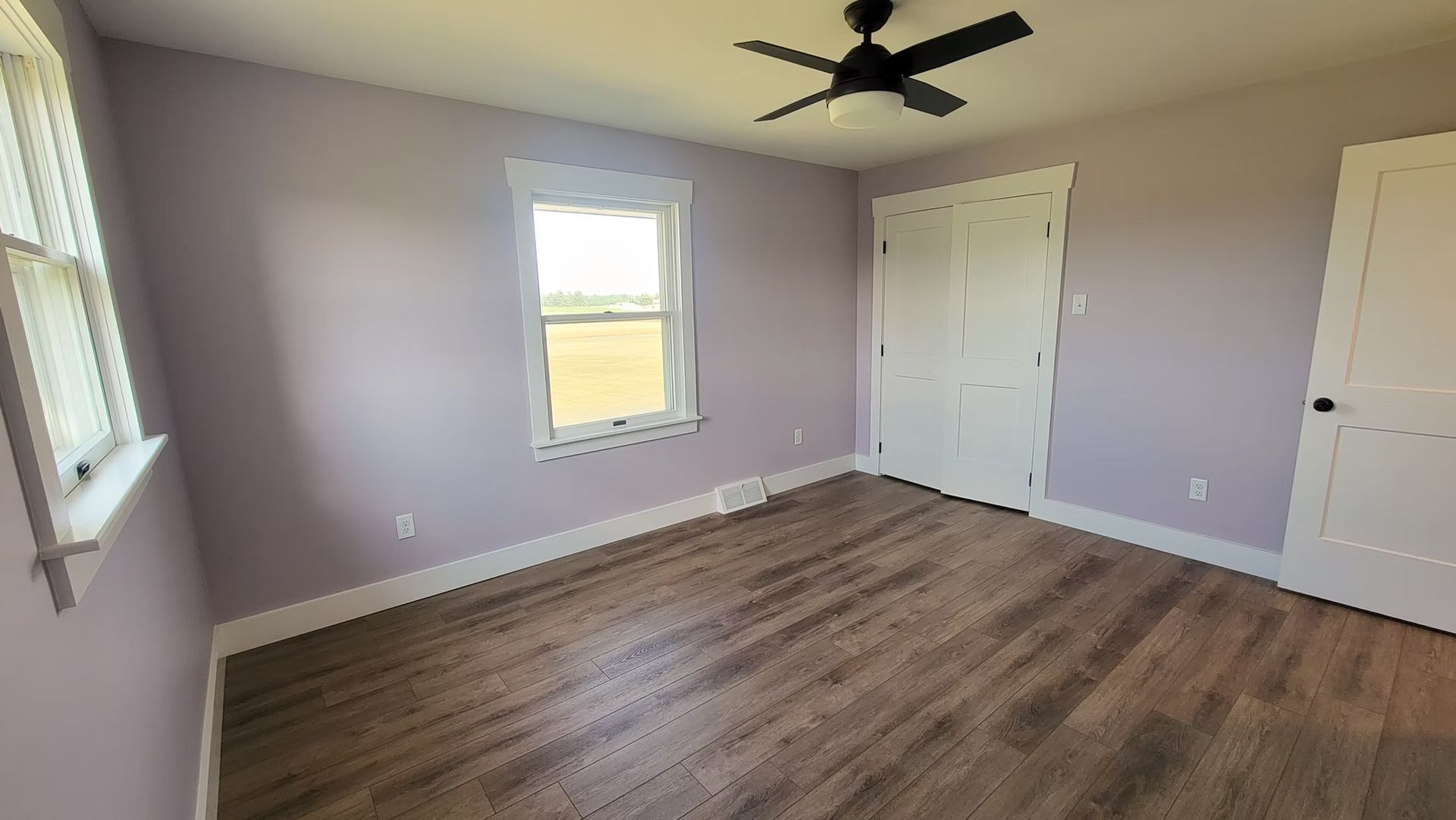 Bedroom with light purple walls, white trim, wood-look floors, and two windows.