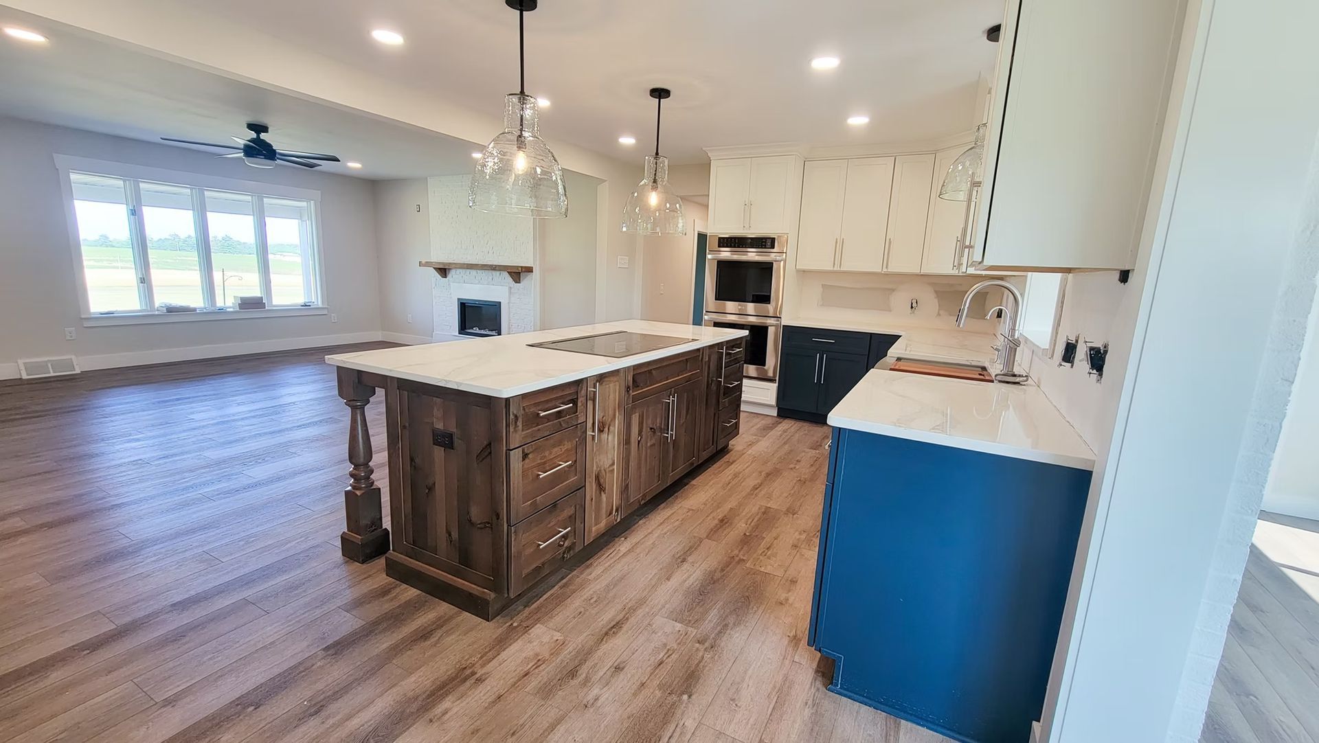 Spacious kitchen with a rustic wood island, white countertops, and blue cabinets; the living area is visible in the background.