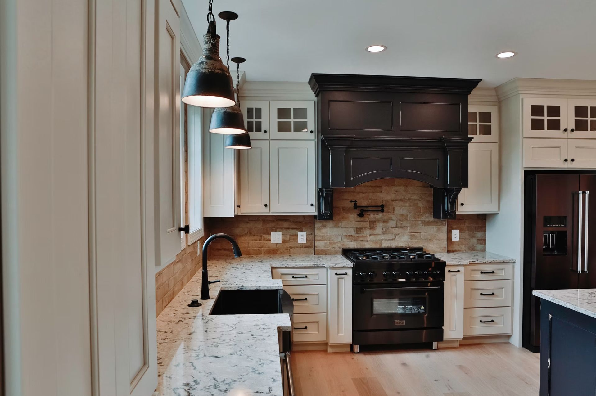 Kitchen with white cabinets, black stove and hood, and wood flooring.