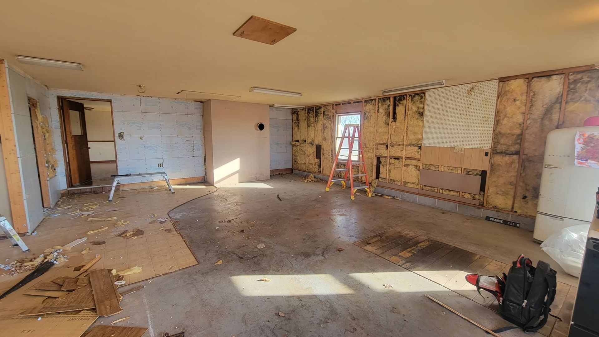 Interior of a room under construction, with exposed walls, debris, and a ladder.