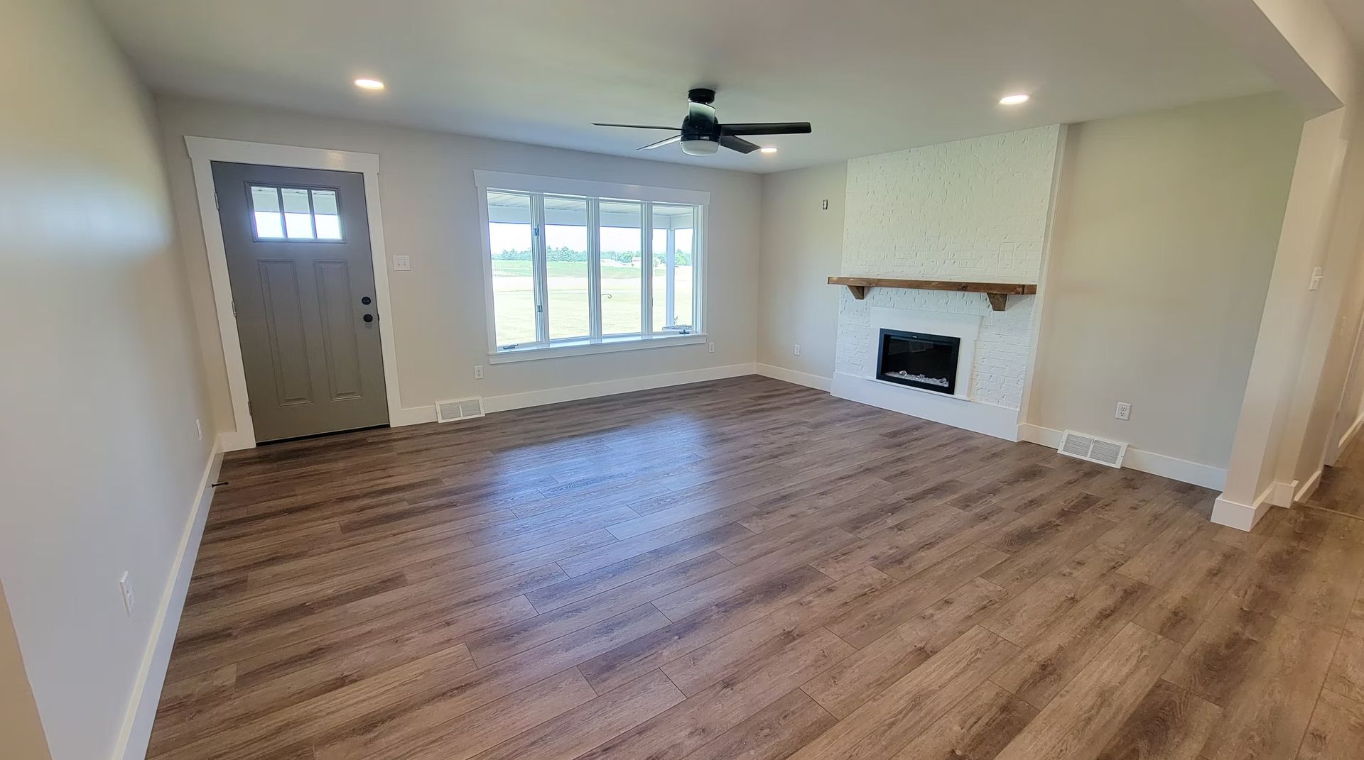 Living room with grey walls, hardwood floors, fireplace, and a large window.
