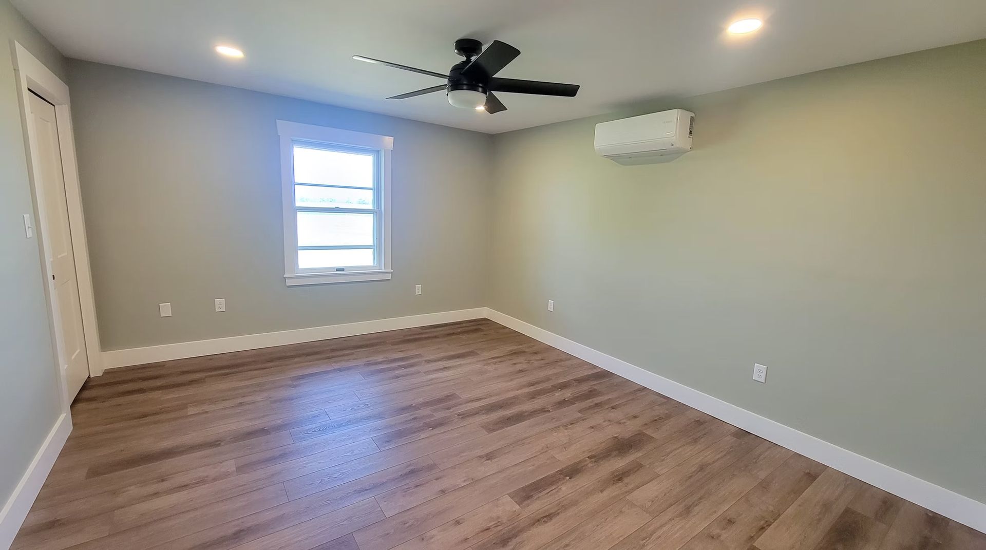 Empty room with wood-look floor, light green walls, window, air conditioner, and ceiling fan.