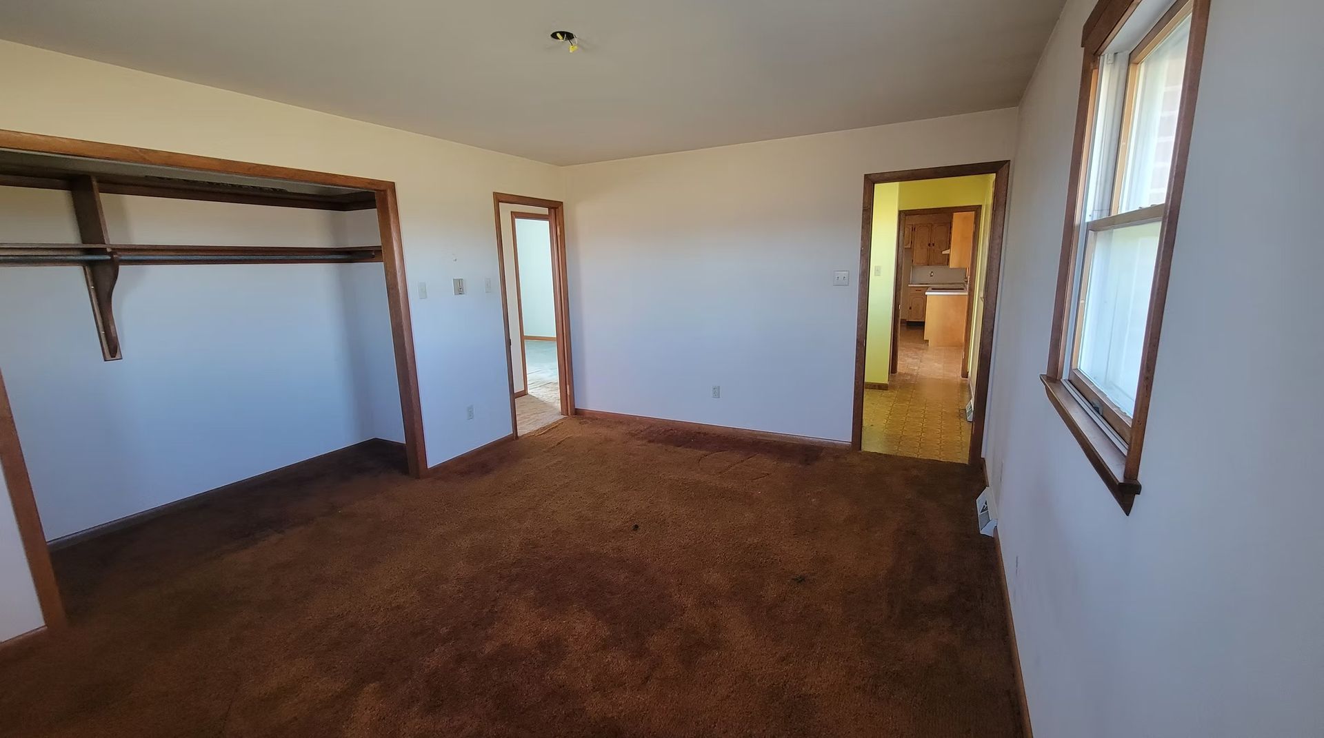 Empty bedroom with brown carpet, closet, and two doorways. One doorway has yellow walls.