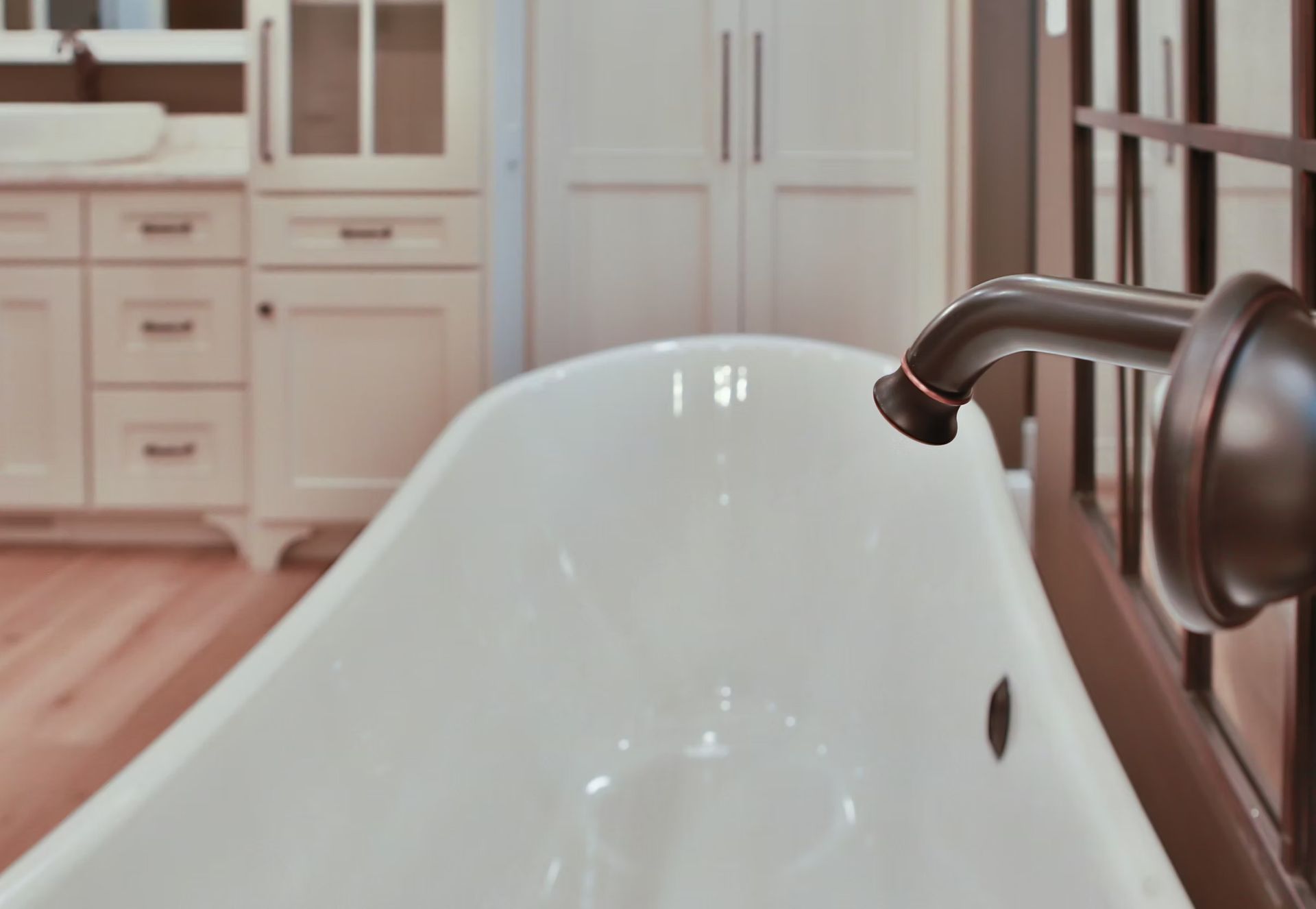 Clawfoot bathtub with bronze faucet, white cabinetry in the background.