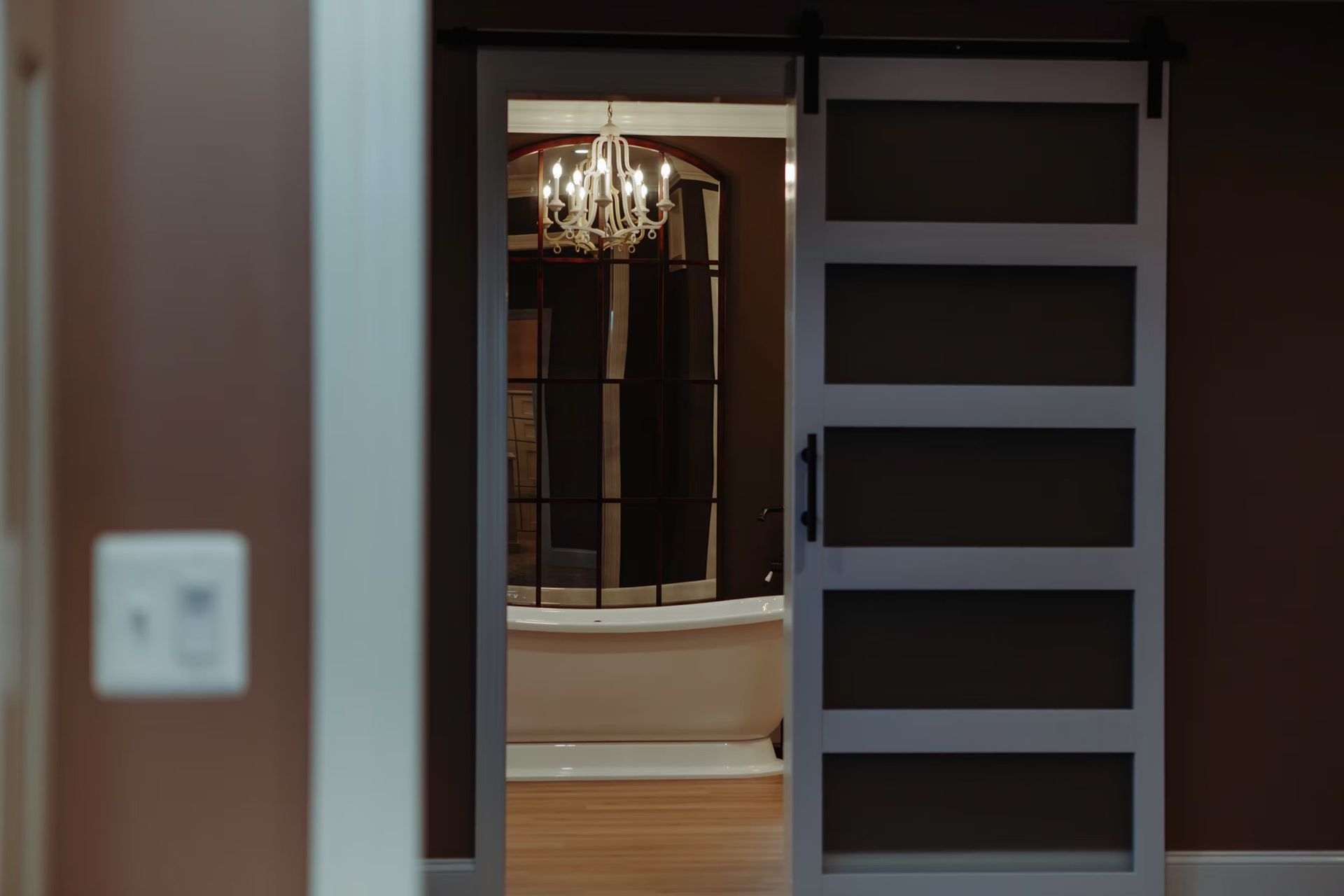 Sliding white door open to a bathroom with a chandelier and a bathtub.