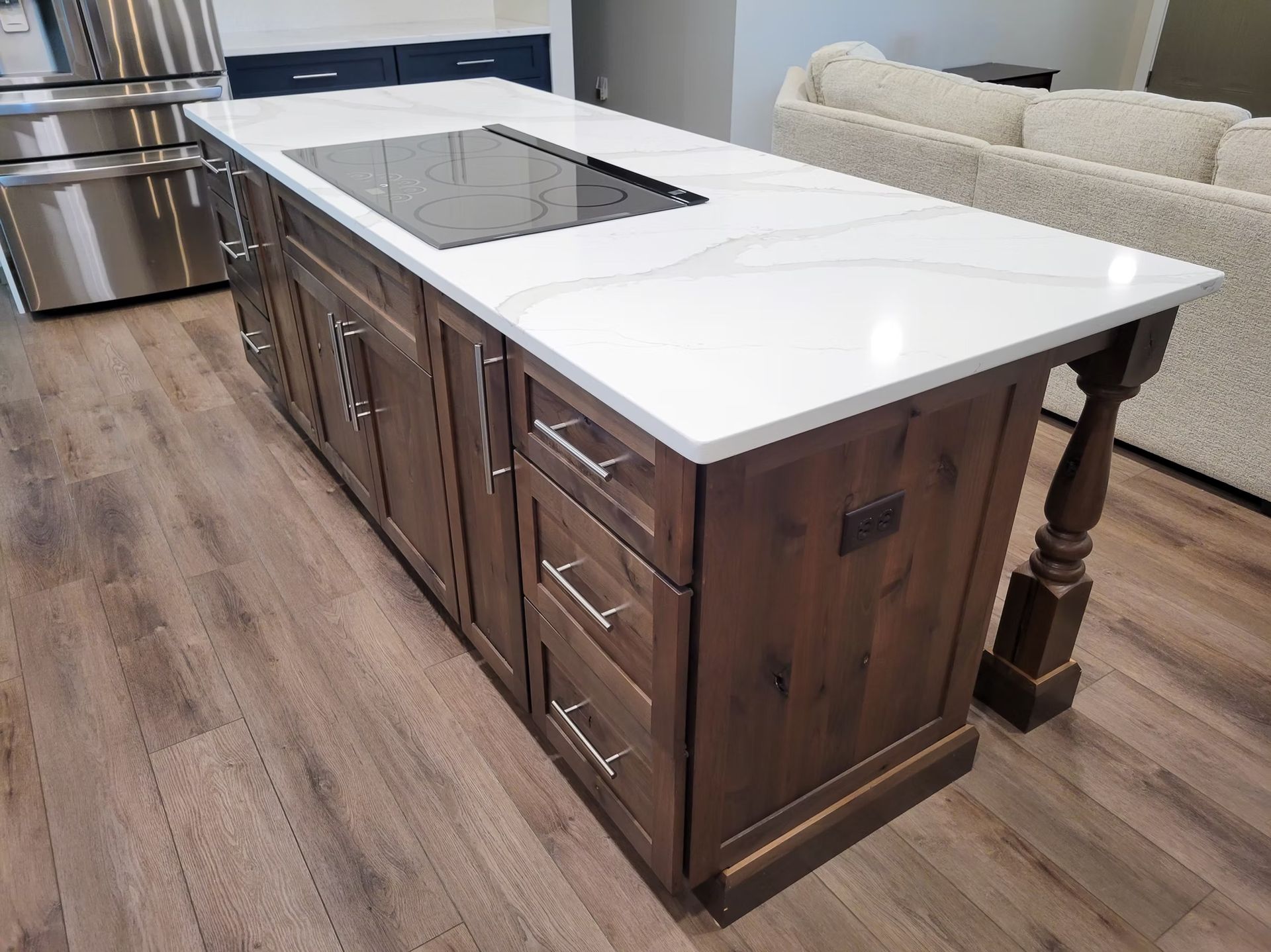 Kitchen island with a white countertop, dark wood cabinets, and built-in stovetop on a hardwood floor.