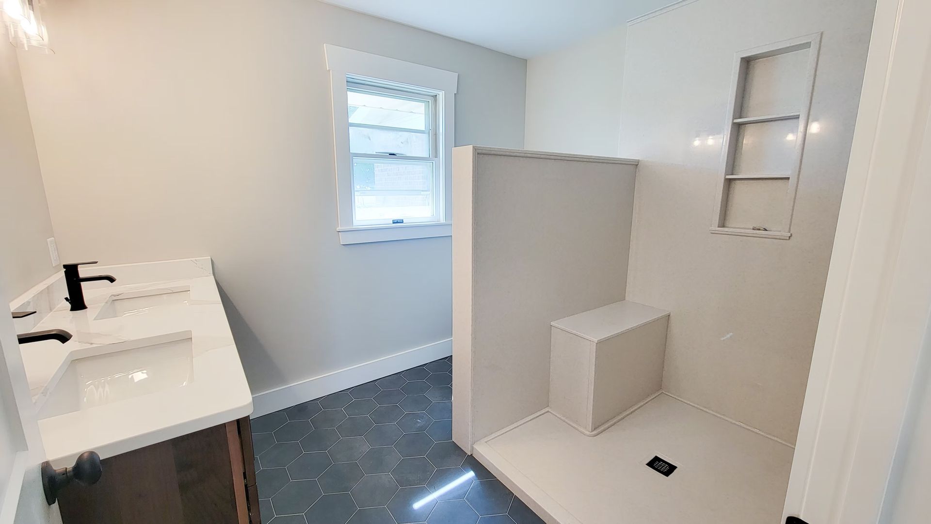 Bathroom with white walls, dark floor, shower with bench, window, and vanity.