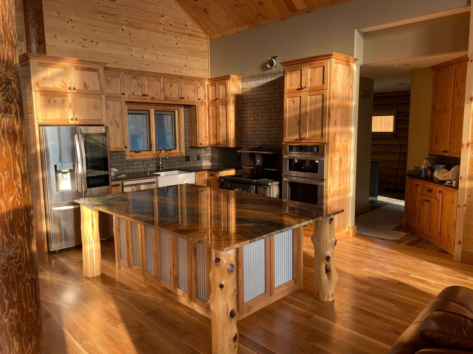 Rustic kitchen with warm wood cabinetry, a large stone-topped island with log-style legs, and stainless steel appliances.