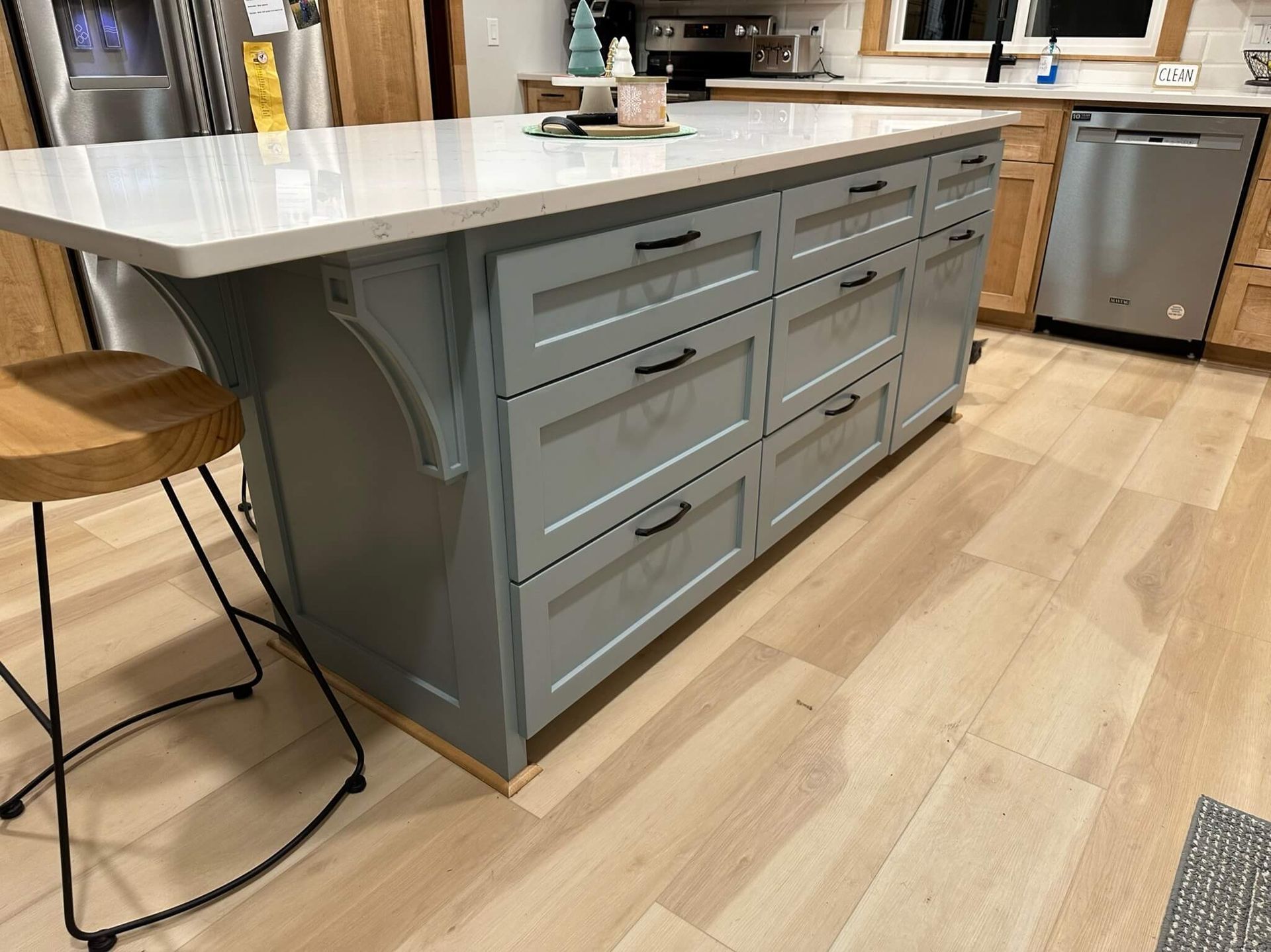 A blue kitchen island with drawers and a white countertop, positioned on light wood flooring next to a bar stool.
